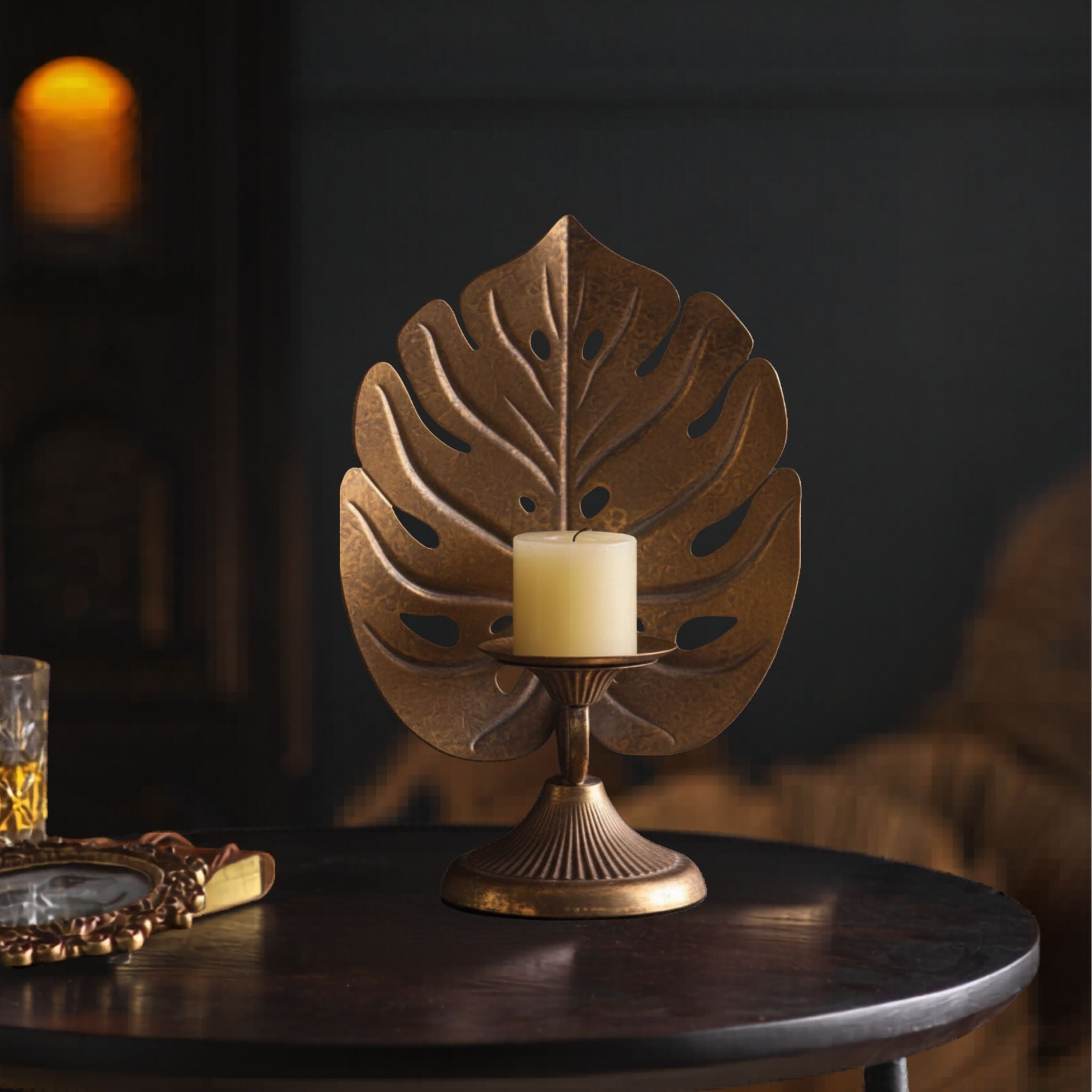 Cleo antique gold monstera leaf pillar candle holder on a round table with a cream candle.