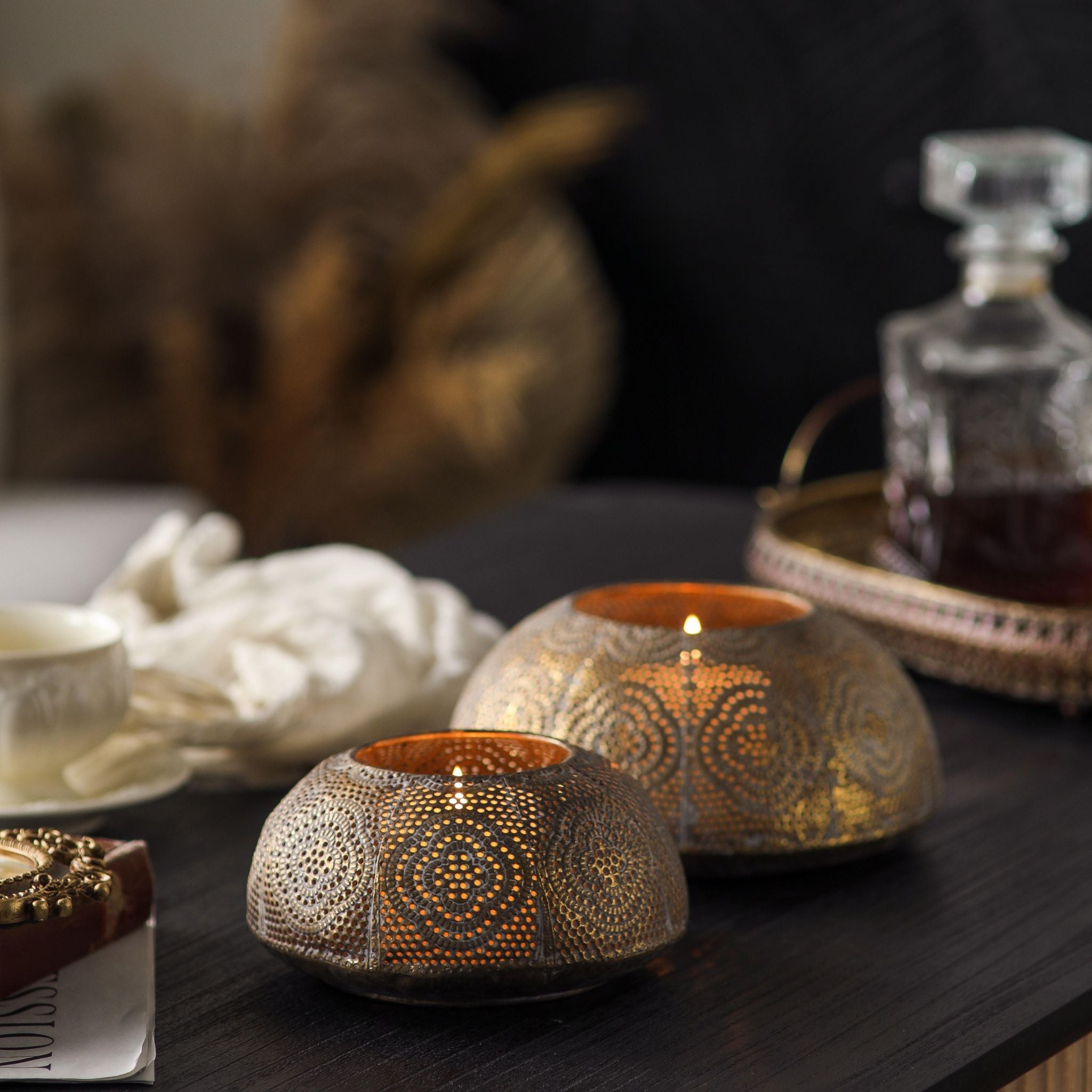 Zahra set of two pierced metal tealight holders lit on a dark table. Hero.