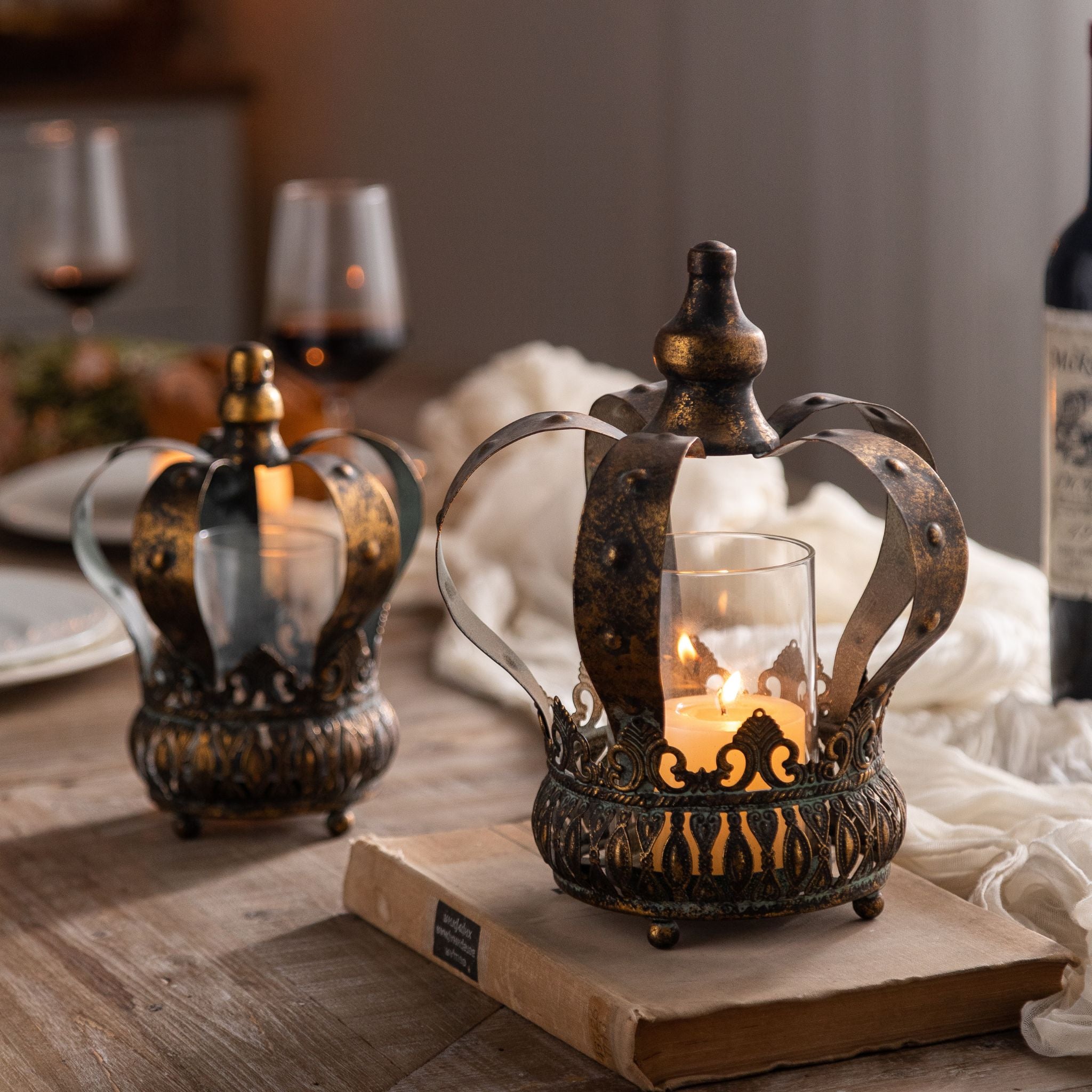 Rhodes crown candle holder pair in an aged bronze finish with glass sleeves on a dining table