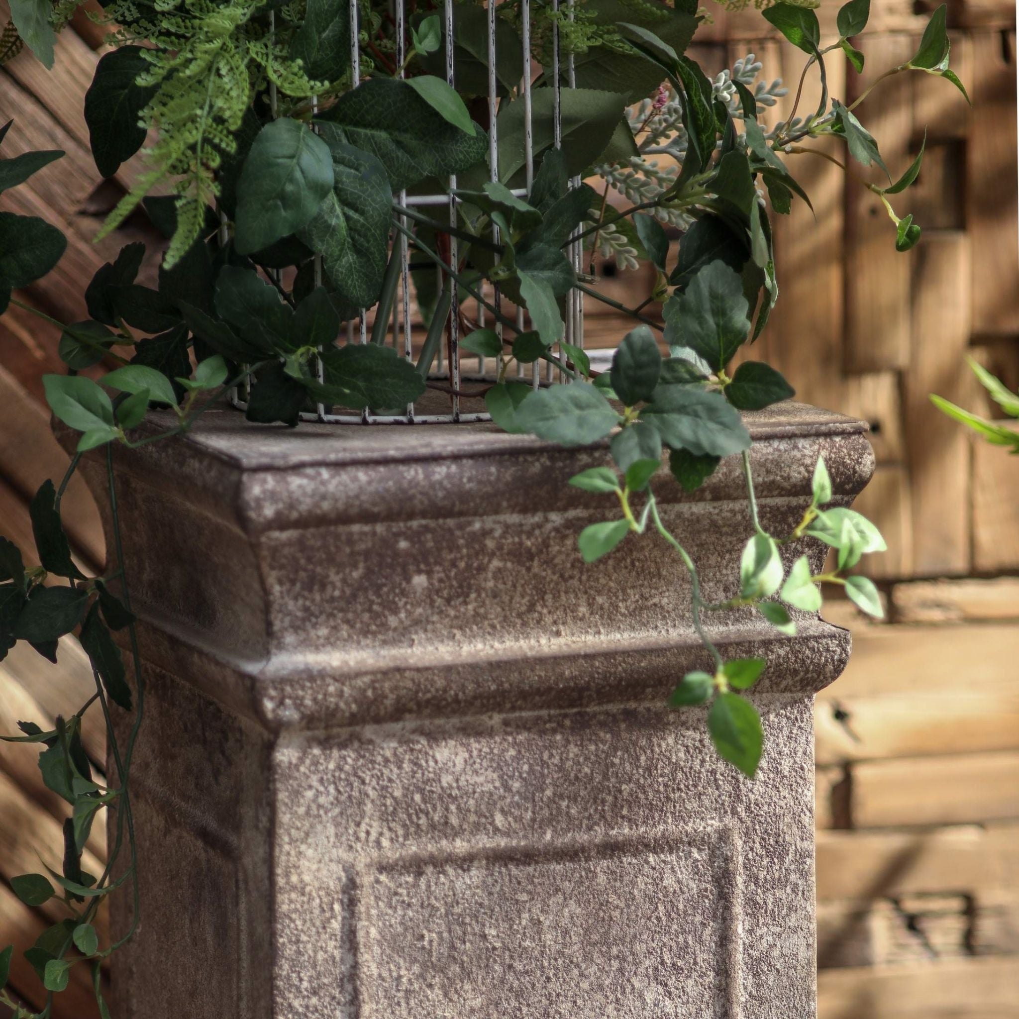 Phoebe pedestal styled on a deck with plants and a garden statue behind