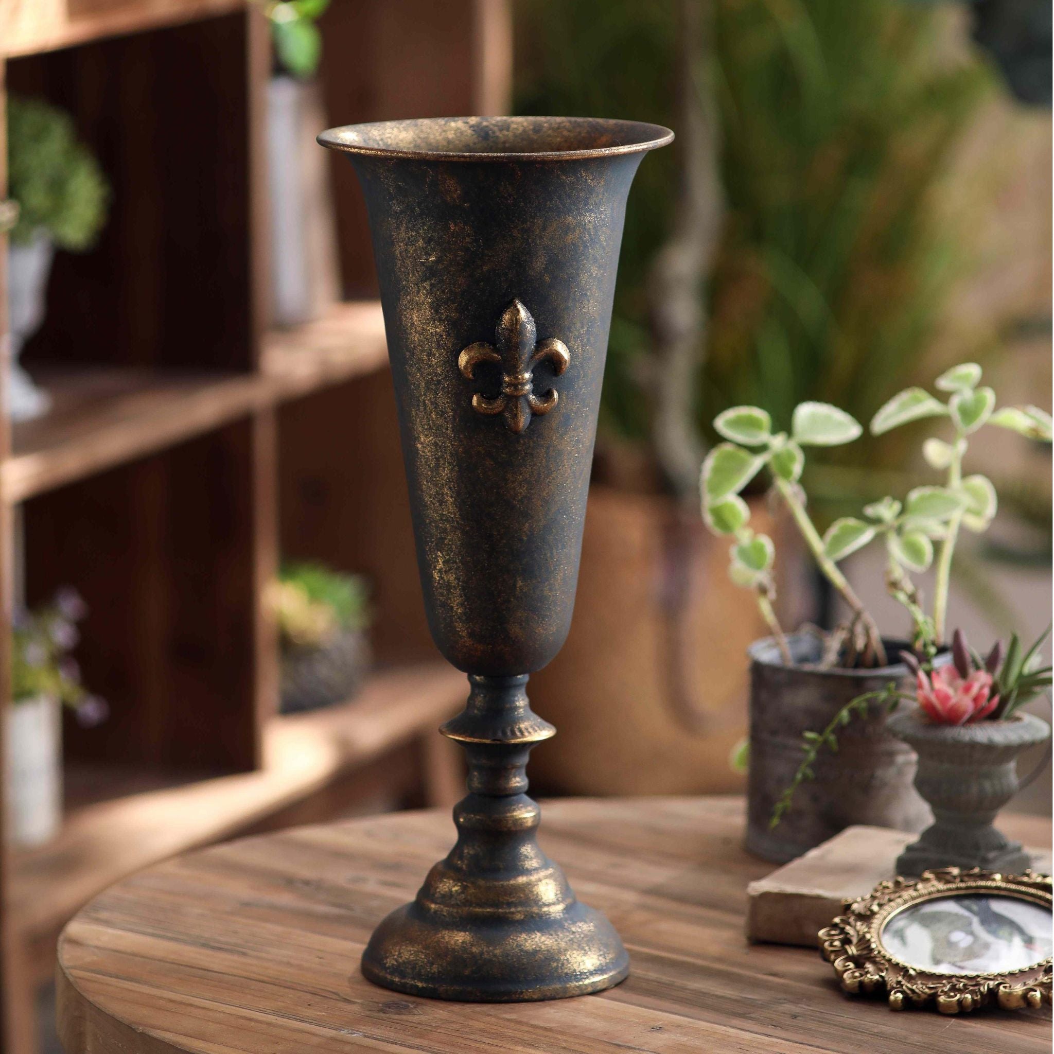 Guido urn vase in aged bronze finish styled on a table beside a gilt frame