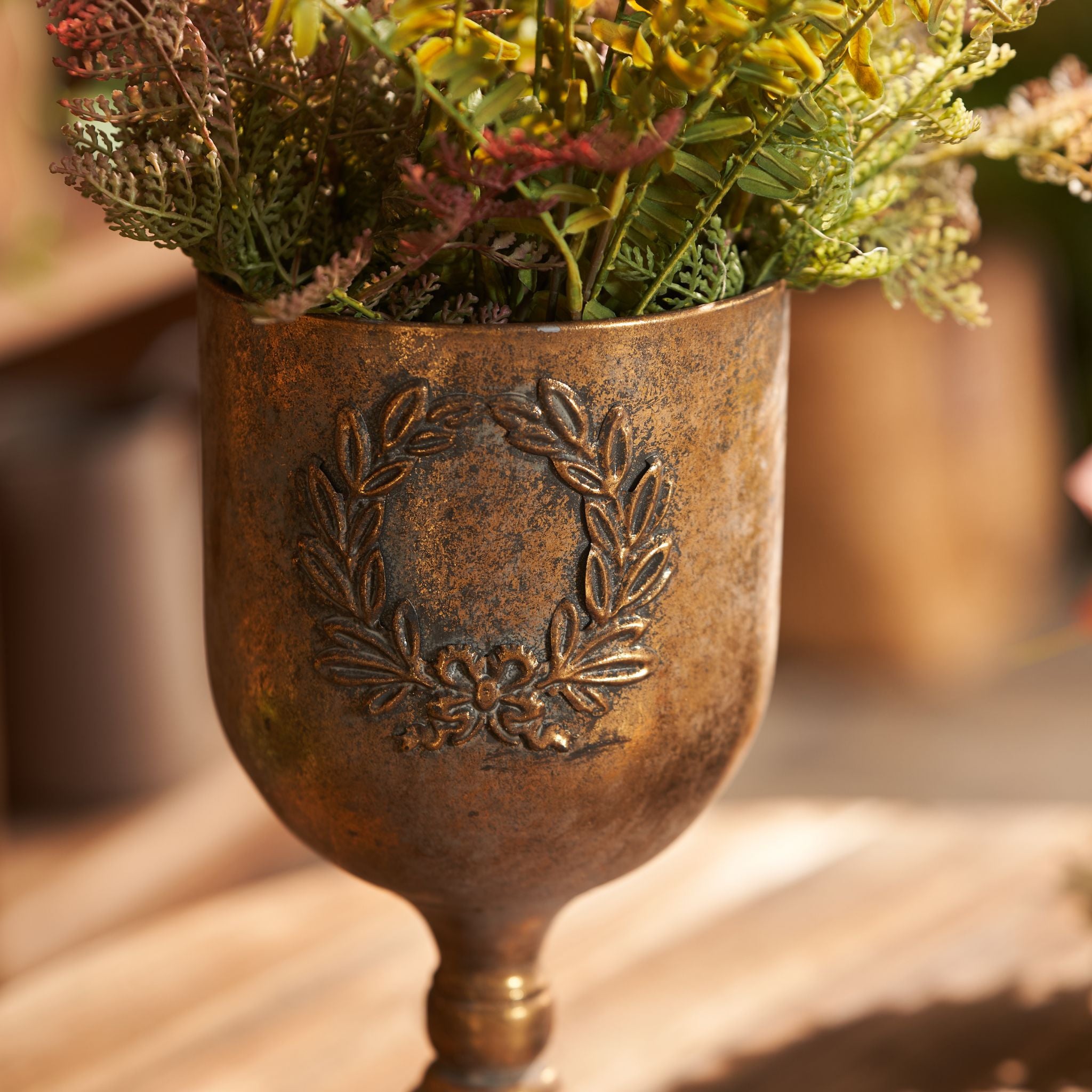 Norma antique gold goblet urn with autumn ferns styled beside a wire cloche