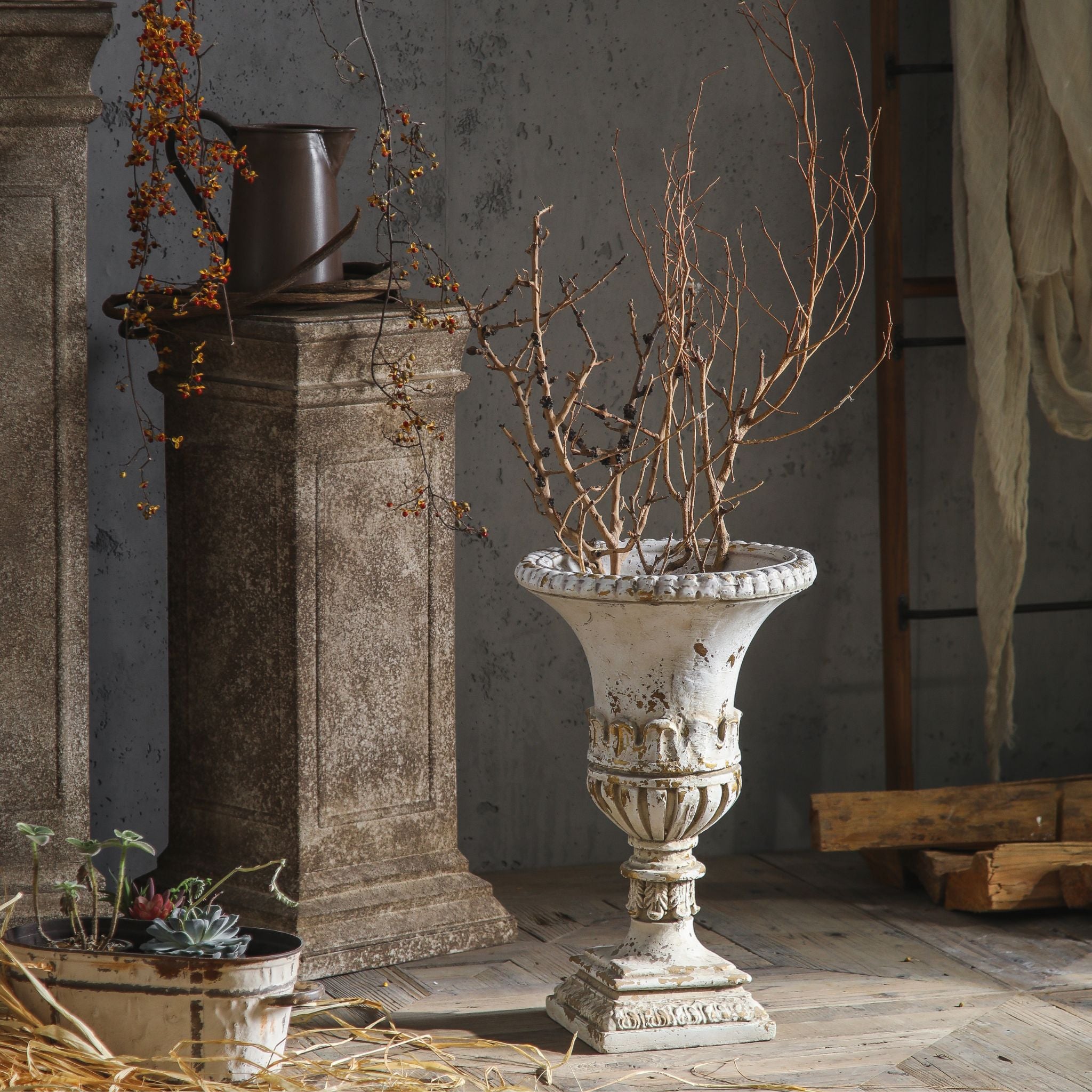 Anaïs French Provincial trumpet urn planter in antique white and gilt, planted with bare branches. Hero.
