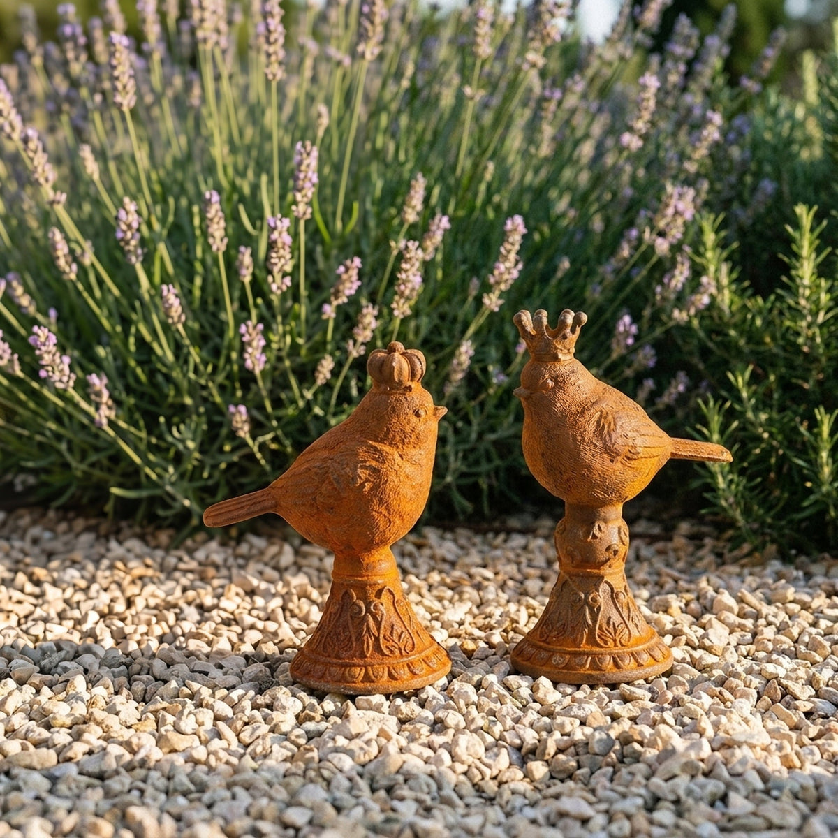 Tom Tit and Jenny Wren rust cast iron crowned bird statues on turned pedestals, on gravel beside lavender