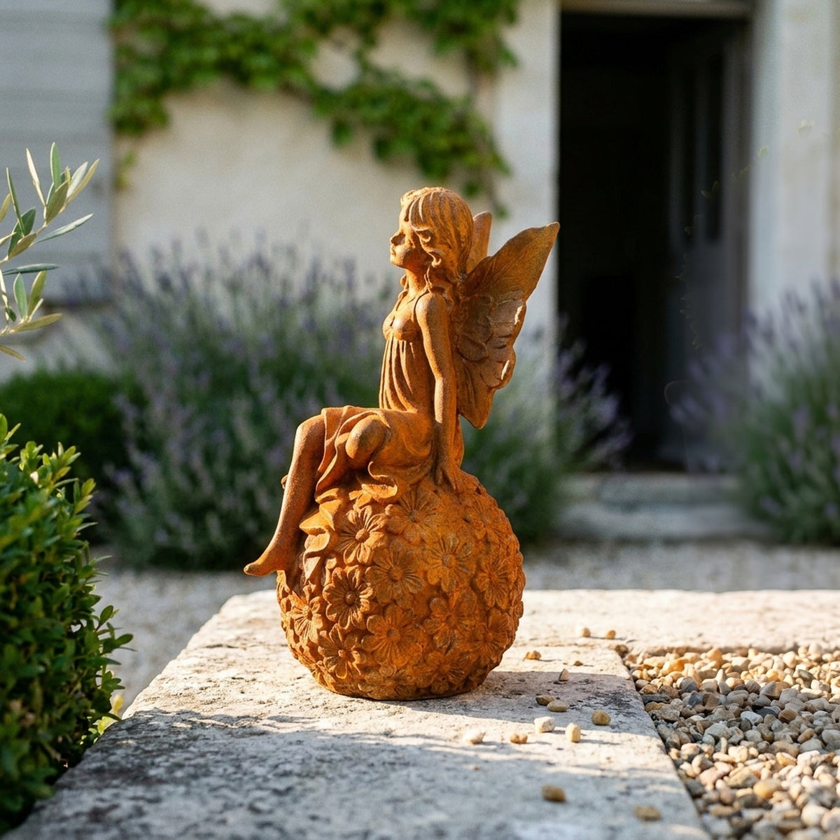 Miss Angelique rust cast iron fairy statue seated on a daisy sphere, on a stone step beside lavender