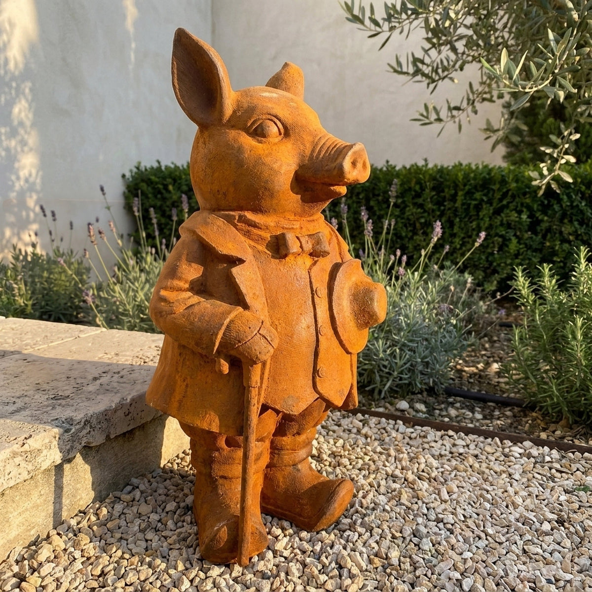 Inspector Truffles large rust cast iron pig statue with cane and hat, on gravel beside lavender