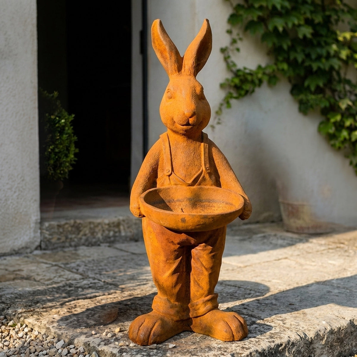 Farmer Barnaby rust cast iron hare statue in dungarees holding a bird feeder dish, standing on gravel