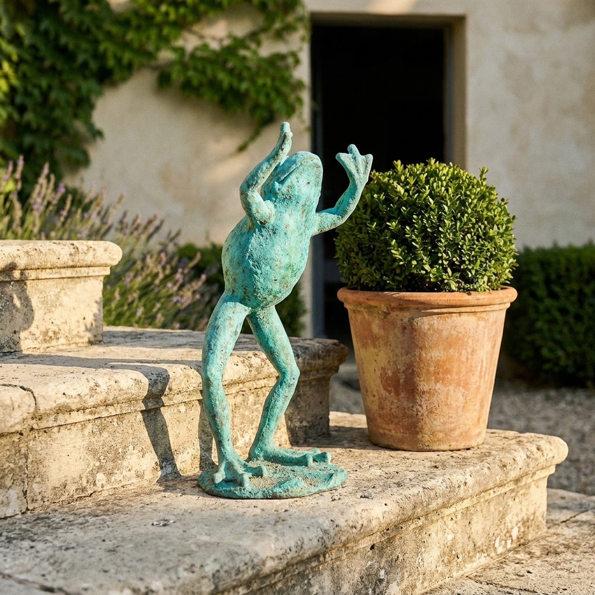 The Frog Prince in bright verdigris cast iron, leaning forward with both arms raised, beside a terracotta pot