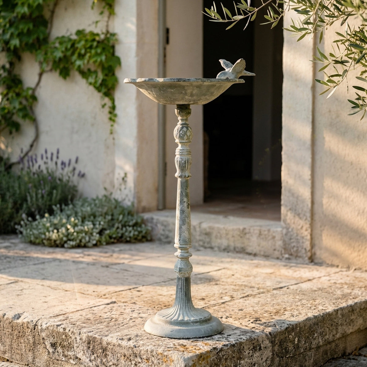 The Willowmere Grey pedestal bird feeder three quarter view in a provencal courtyard