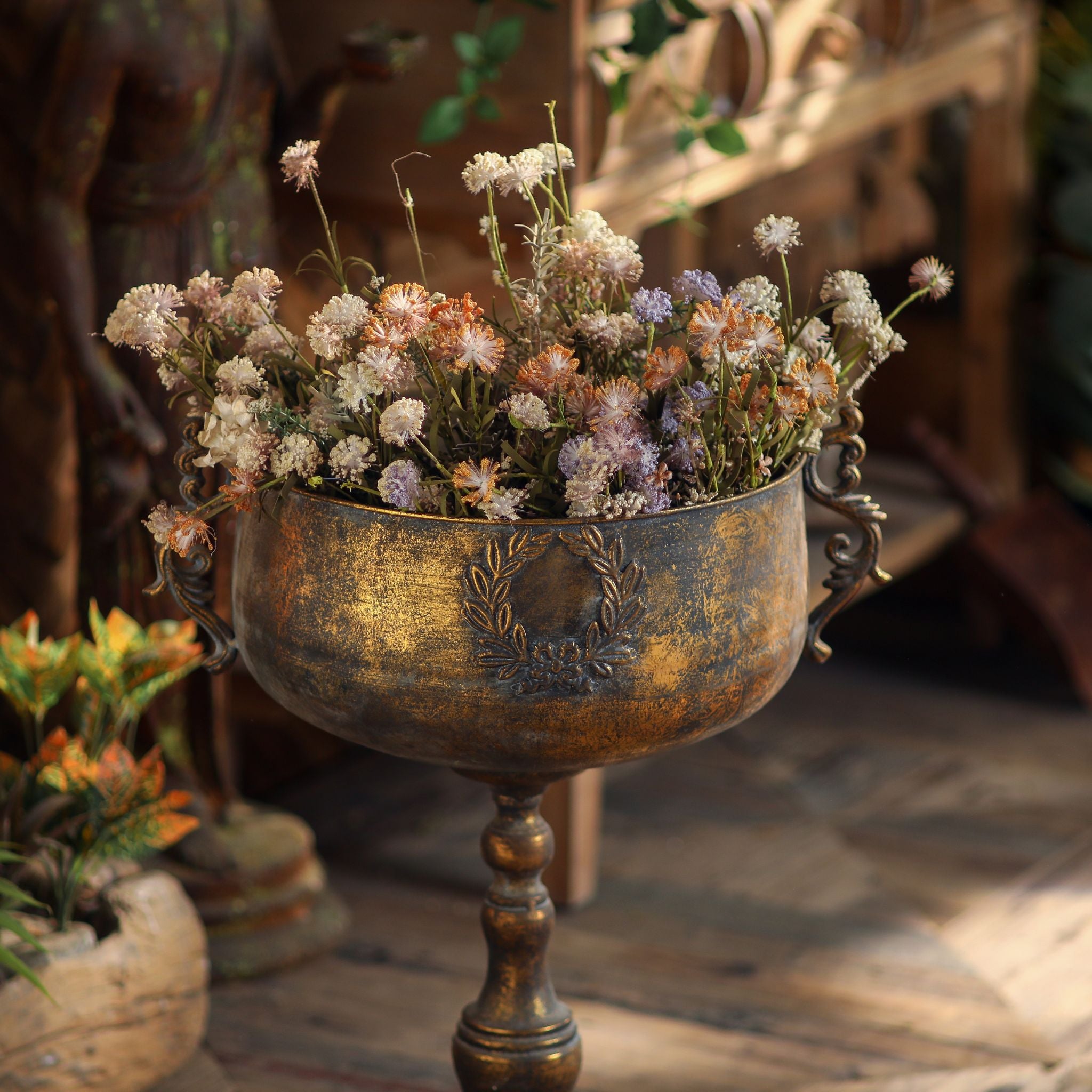 Close angle of the antique gold urn planter with dried flowers, showing the laurel crest and scroll handle detail
