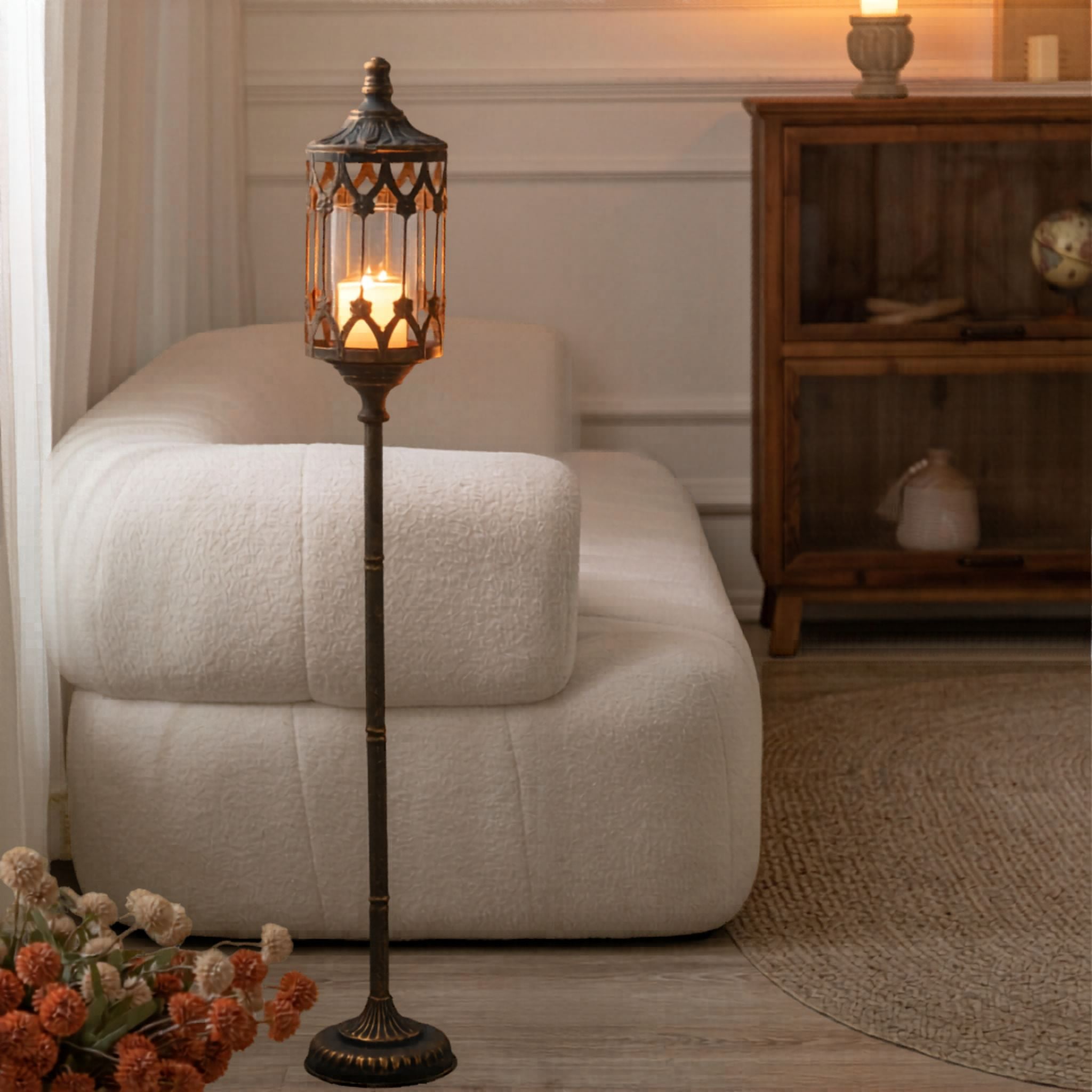 Tall floor candle lantern glowing beside a sofa in a styled room