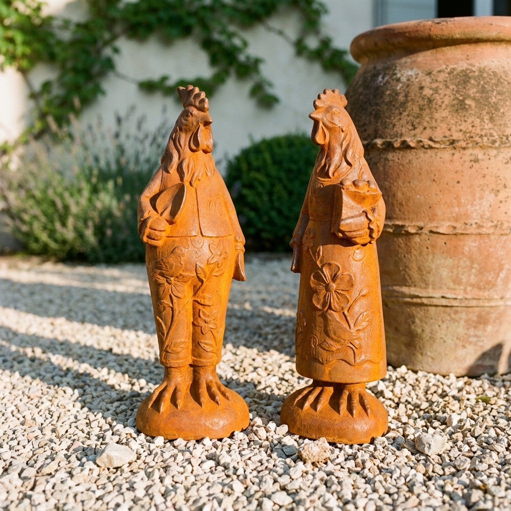 Mr Featherwick and Mrs Cluckington rust cast iron rooster and hen statues standing together on gravel beside a terracotta pot