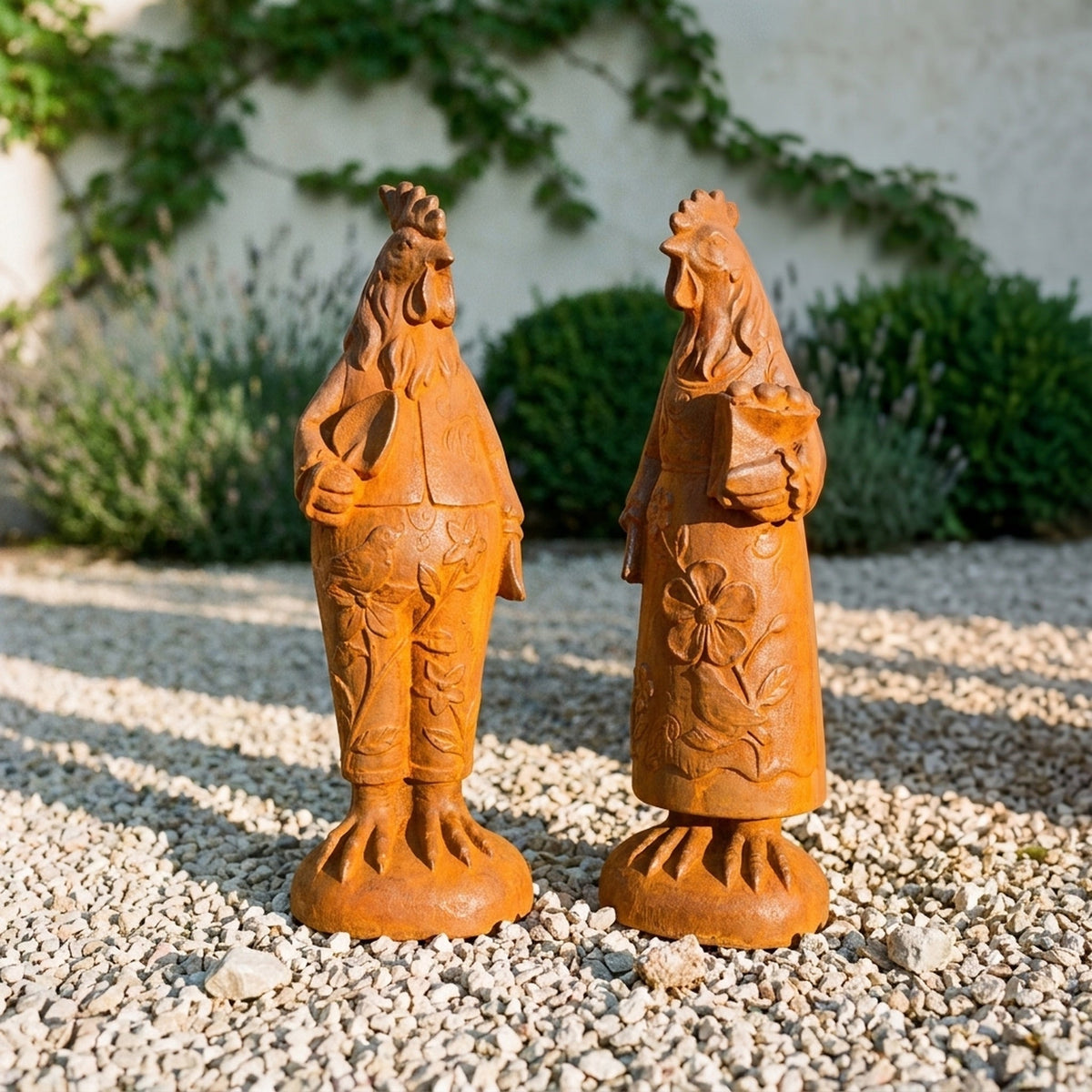 Mr Featherwick and Mrs Cluckington rust cast iron rooster and hen statues standing together on gravel beside lavender