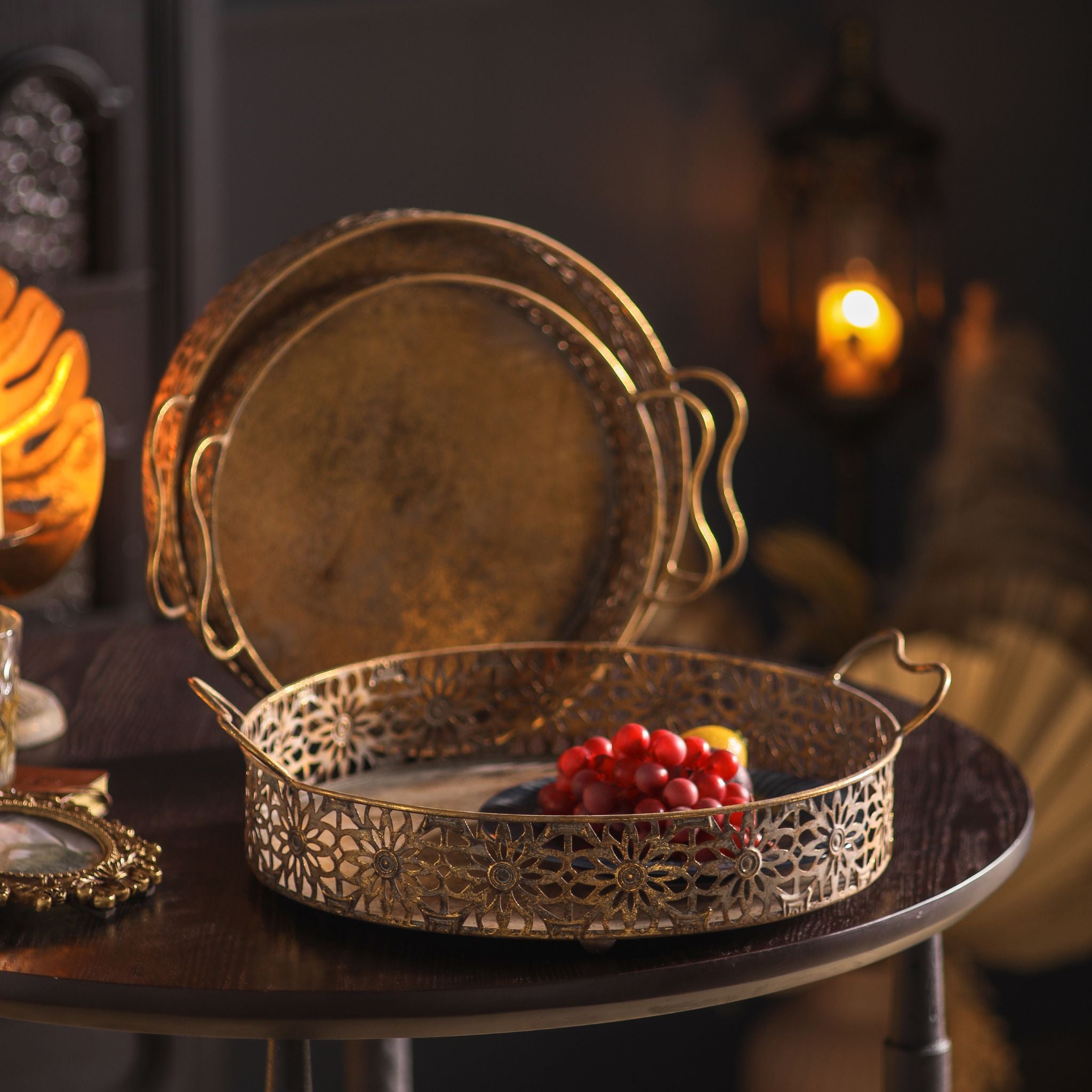 Paolo French Provincial round tray set of 3 in pierced floral metal, whitewashed gold, styled with fruit on a dark table. Hero.