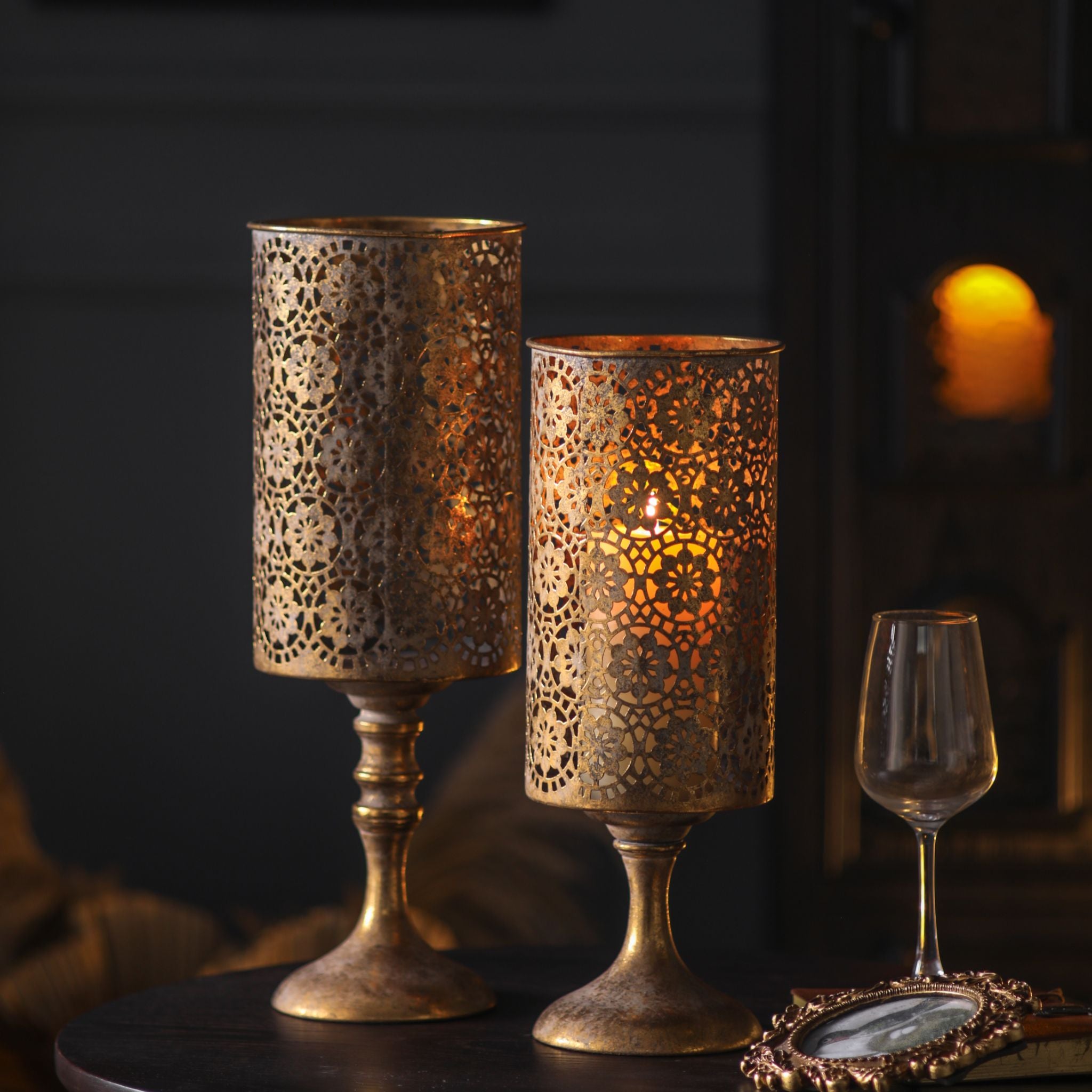 Paros French Provincial candle holder set of 2 in pierced lace antique gold, both lit on a dark table. Hero.