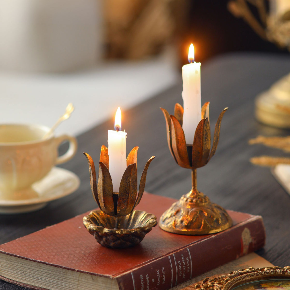 Massimo gilded flower candle holder set of 2 with lit taper candles on a vintage book. Hero.