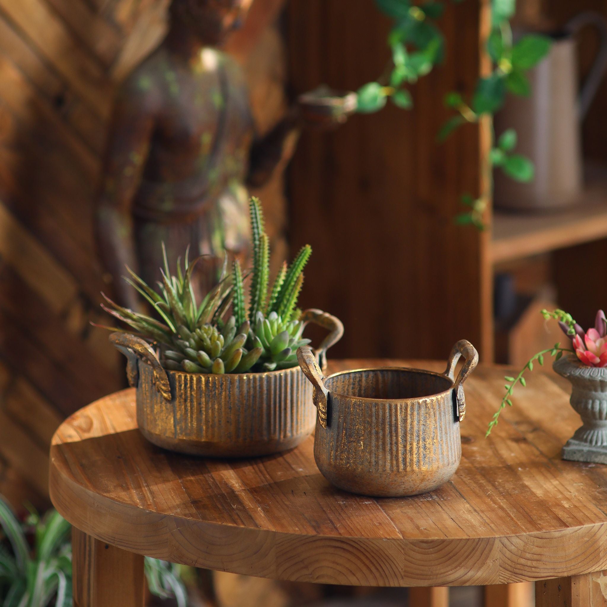 Milo planter pot set of 2 in ribbed worn gold with handles on a round timber table. Hero.