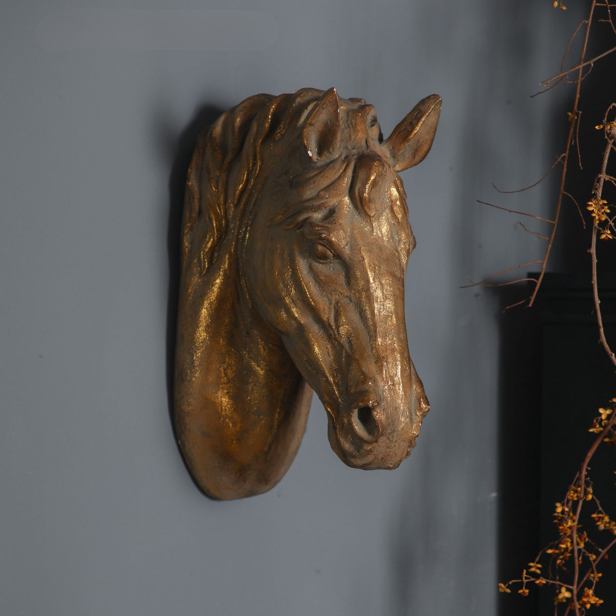 Cara horse head wall sculpture in aged gold magnesia mounted on a grey wall. Hero.