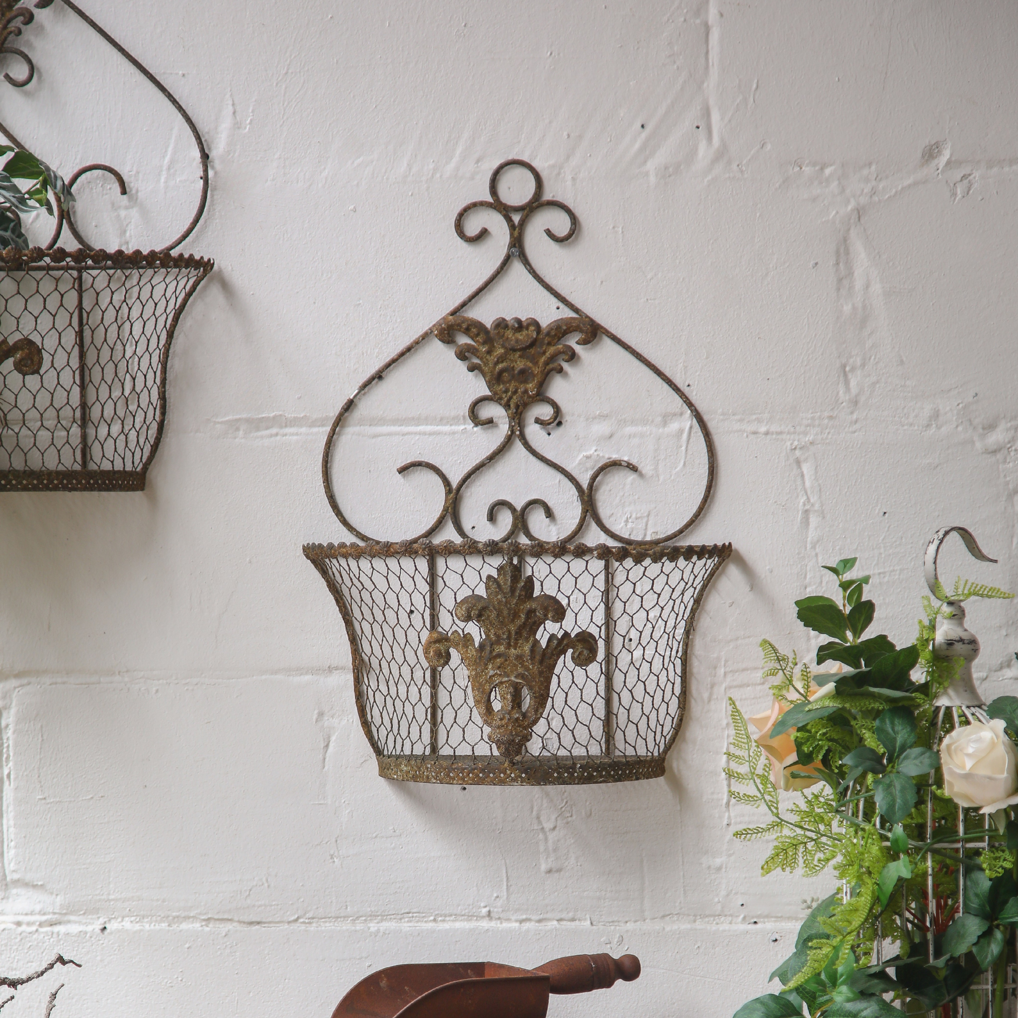 Como wire wall basket planter with scrolled heart crown on a white brick wall. Hero.