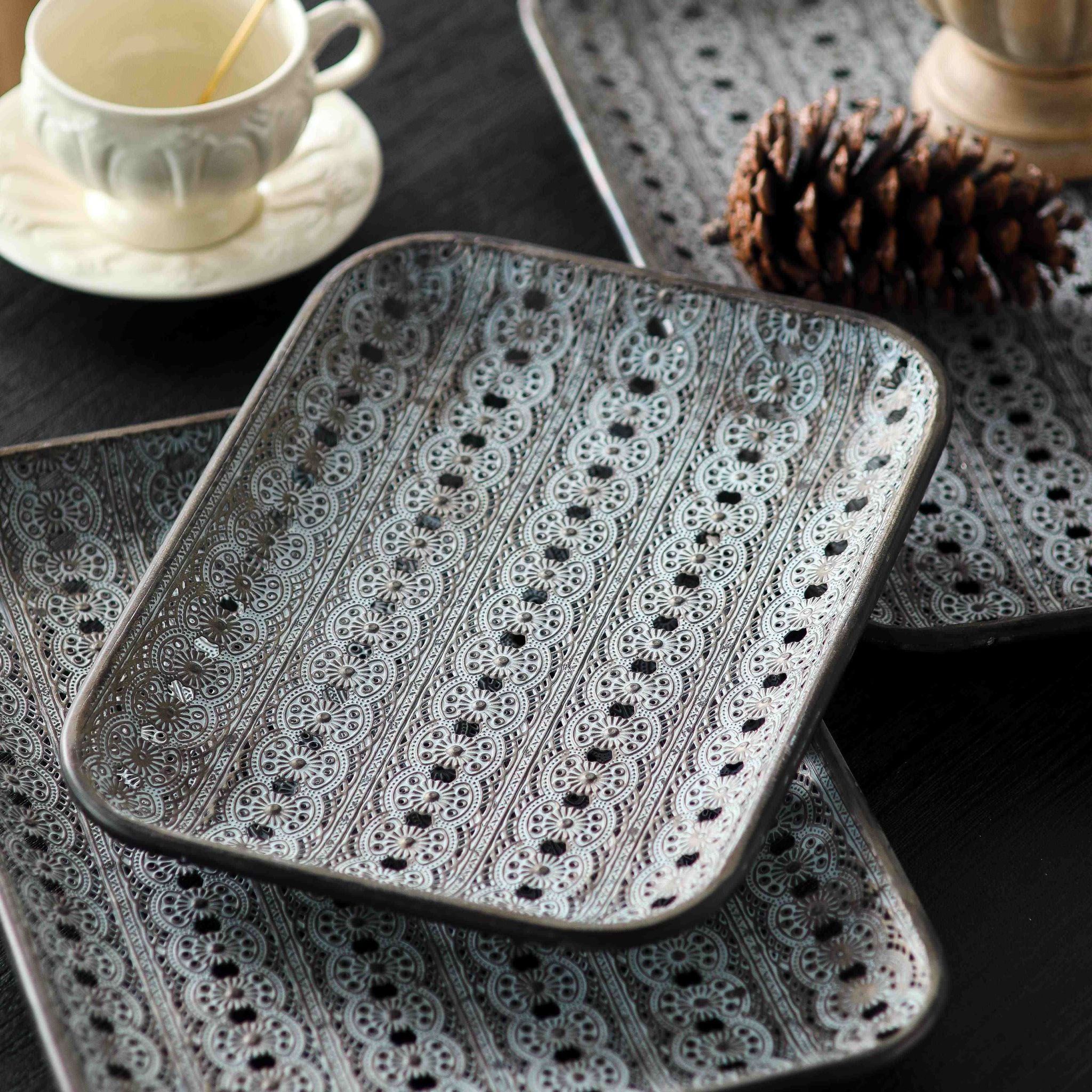 Adélaïde metal trays stacked in graduated sizes, the smallest tray on top, whitewashed grey lace pattern