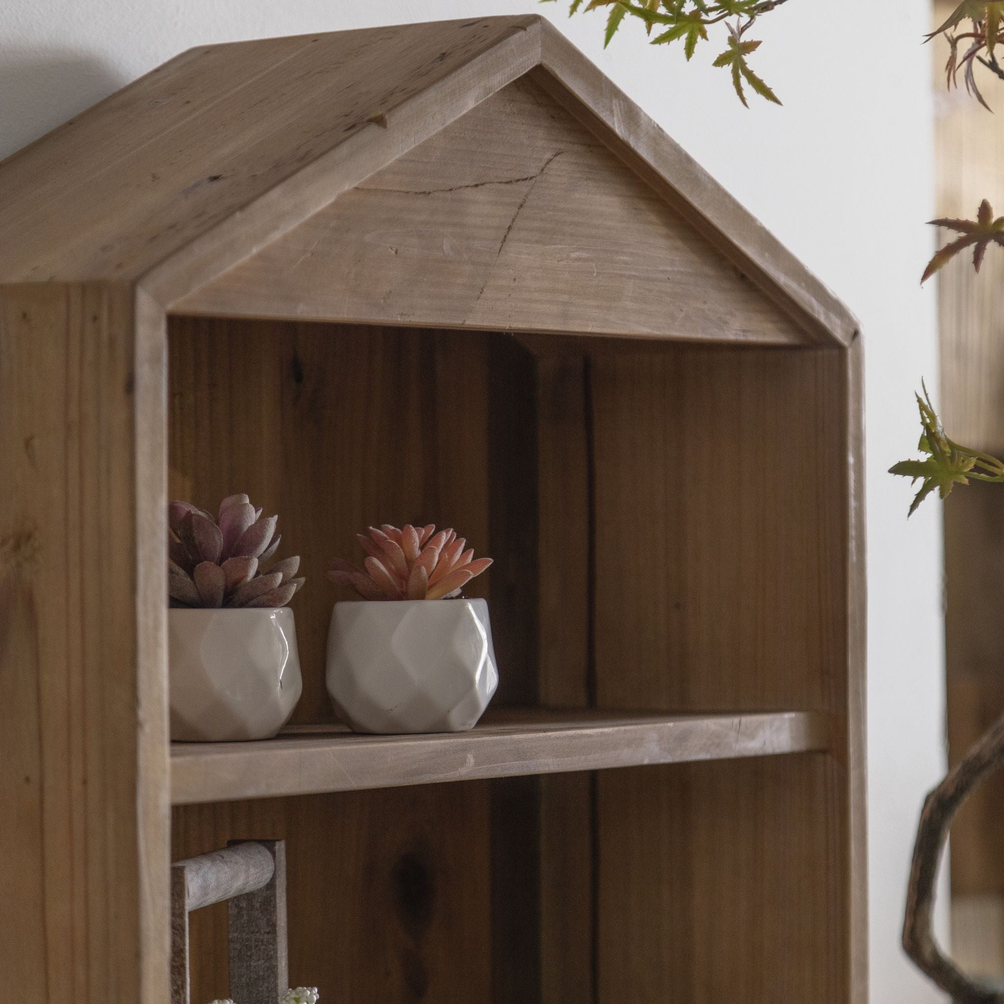 Alderic wall shelf, detail of the gabled peak and upper shelf with two potted succulents.