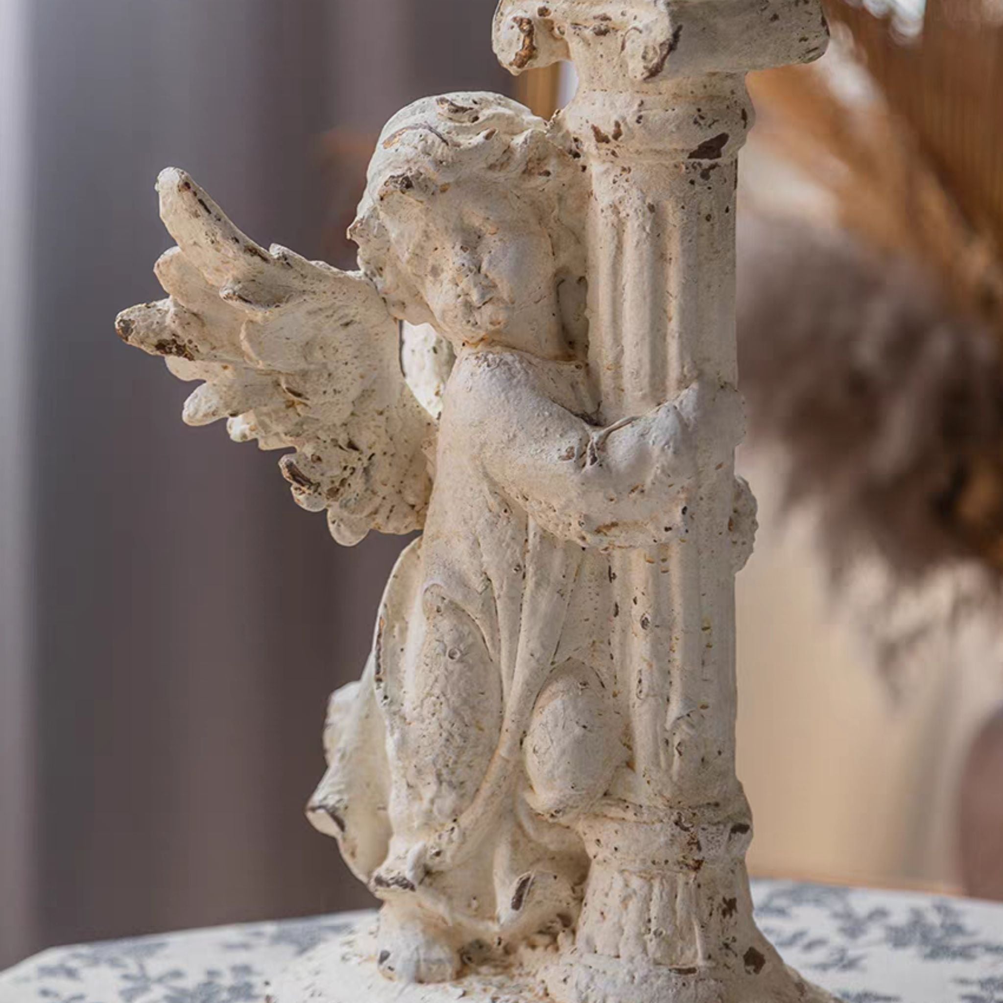 Close-up of the André cherub's wing, hair and arms gripping the fluted column in distressed antique white.
