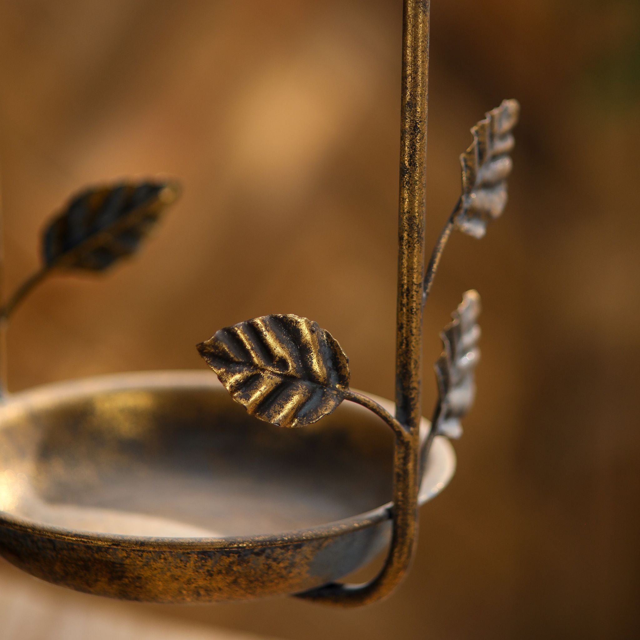 Close-up of the leaf detailing and seed dish on the Nathalie antique gold bird feeder.