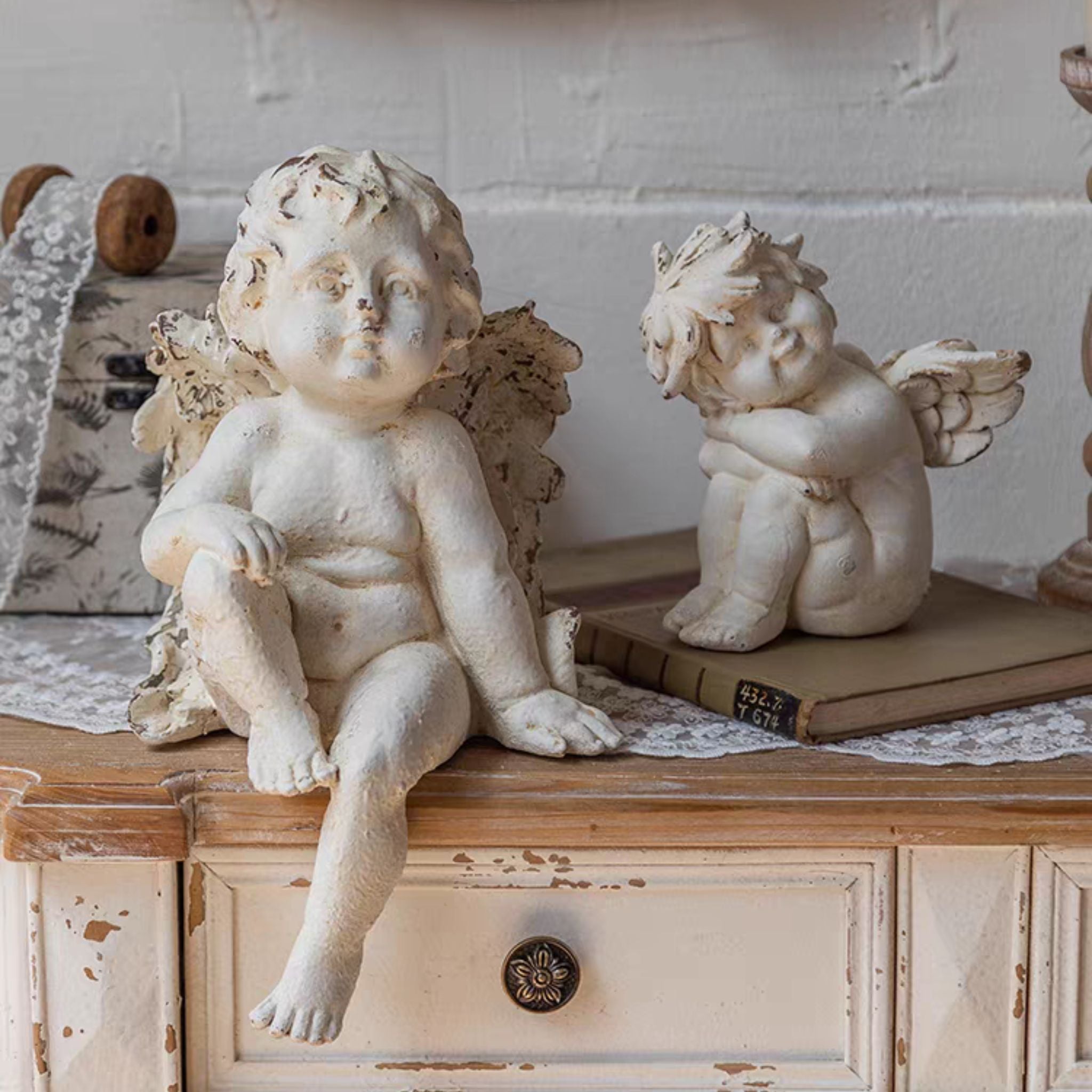 Antoine cherub figurine seated with a smaller cherub knees-tucked beside him on a stack of vintage books