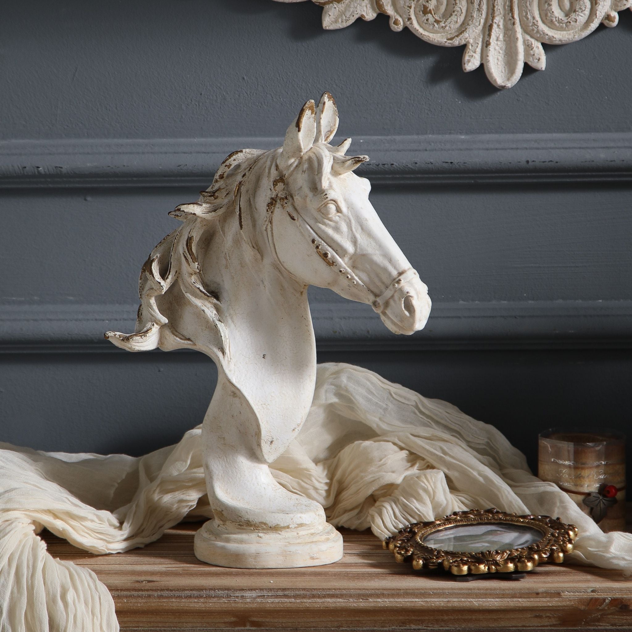 Apollon French Provincial horse head bust sculpture in distressed white finish on turned pedestal base, styled on a wood console with cream cheesecloth, ornate gilt picture frame, and antique candle. Hero