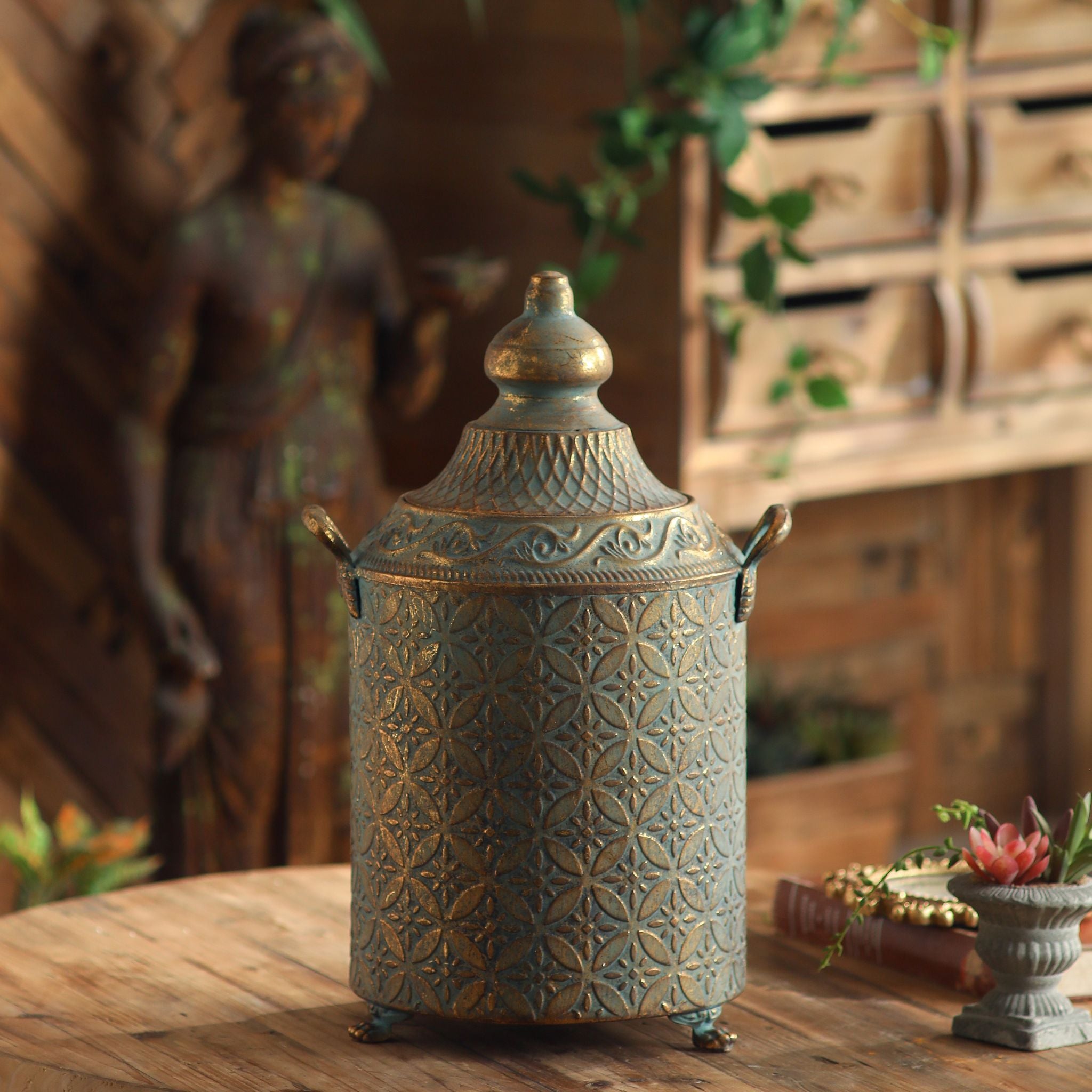 Aria French Provincial tall lidded canister in antique gold over verdigris embossed metal, with domed finial lid and twin handles. Hero.