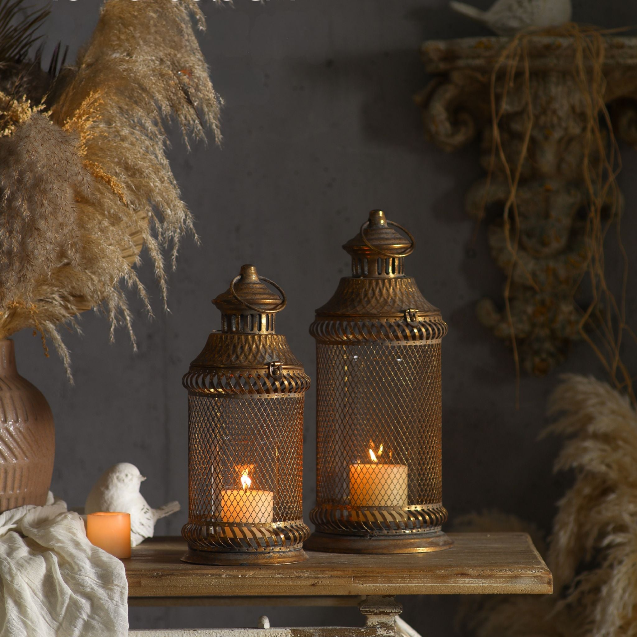 Arielle lantern, taller on the right, shown beside the shorter Melissa lantern on a timber table, both lit. Sold separately.
