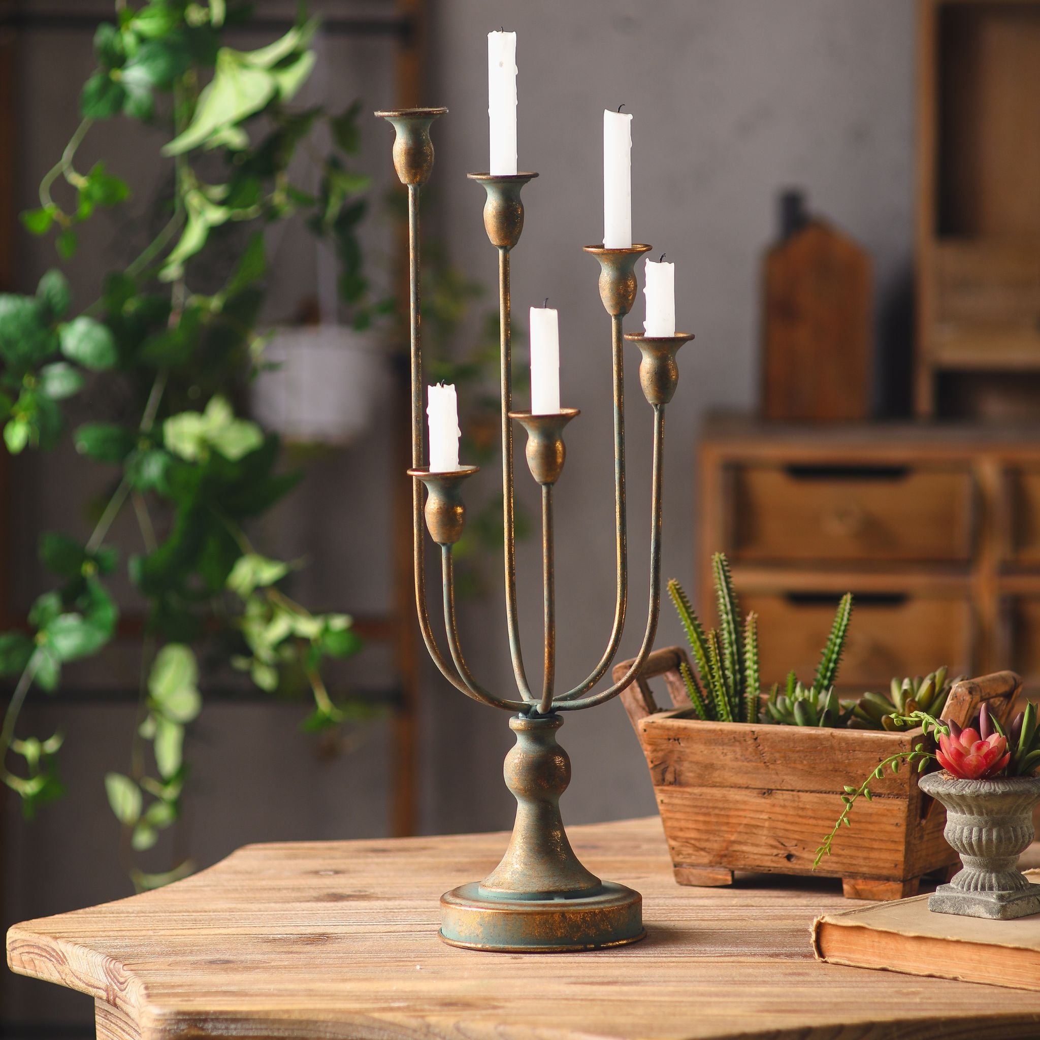 Audrée six-arm table candelabra shown full with unlit taper candles, antique gold worn over a verdigris base, staggered trumpet cups.