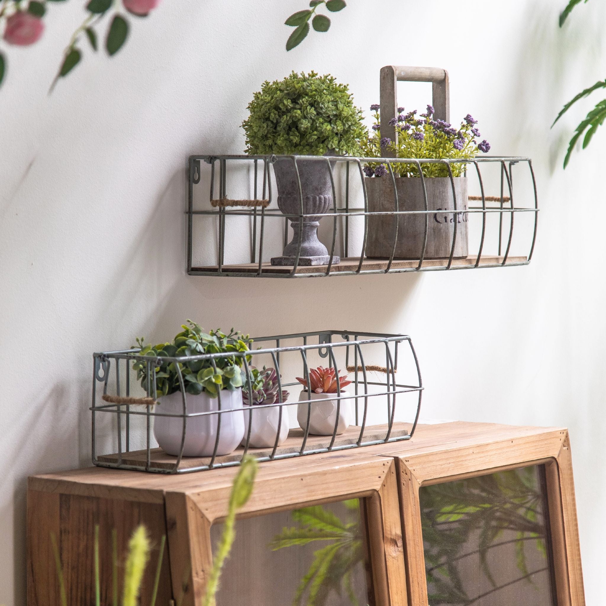 Aurelie set of two aged wire wall baskets, one hung and one on a cabinet, styled with potted plants.Hero