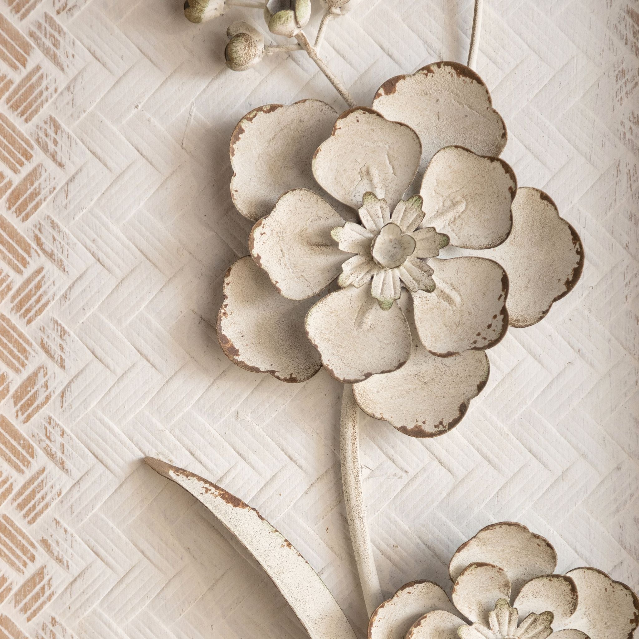 Close-up of a raised metal flower on the Aurélien panel, distressed cream with aged edges.