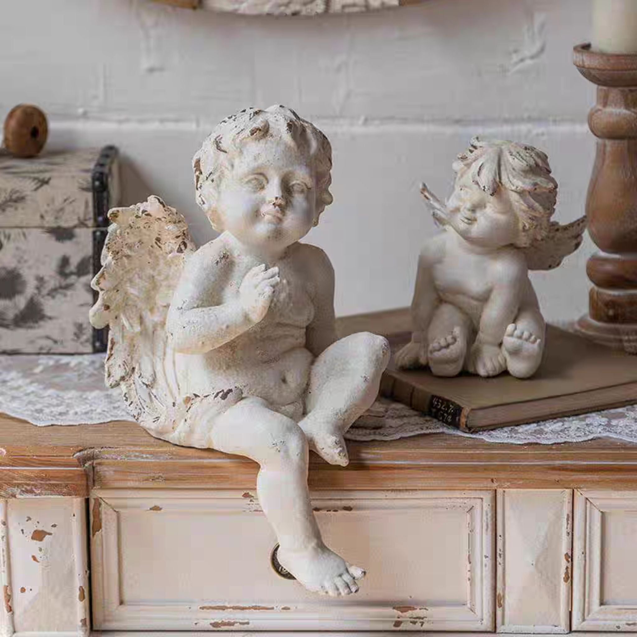 Bastien French Provincial cherub figurine in distressed whitewash, sitting on a vintage book with a second cherub to the left.