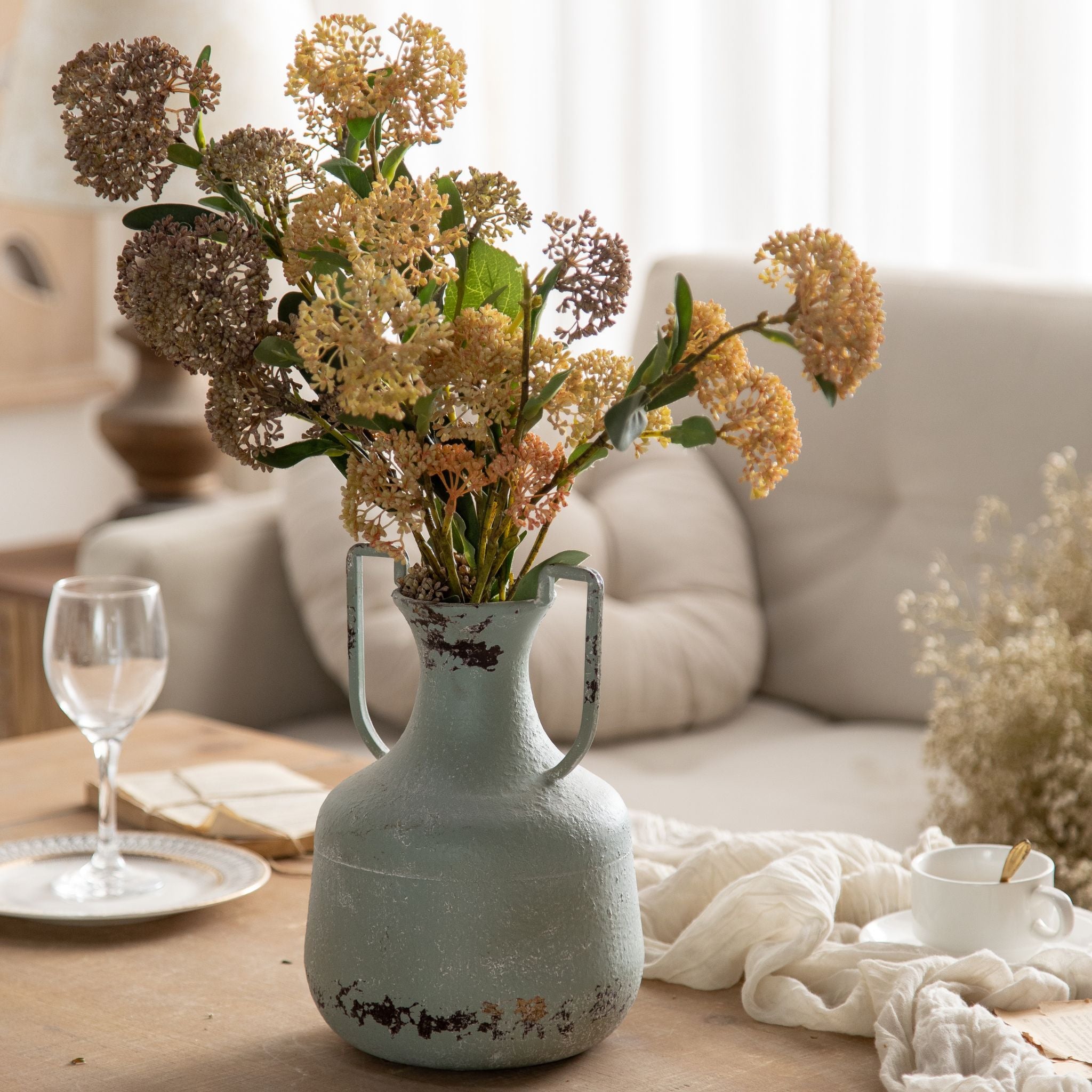 Beau distressed sage amphora vase with twin handles, holding dried stems on a coffee table. Hero.