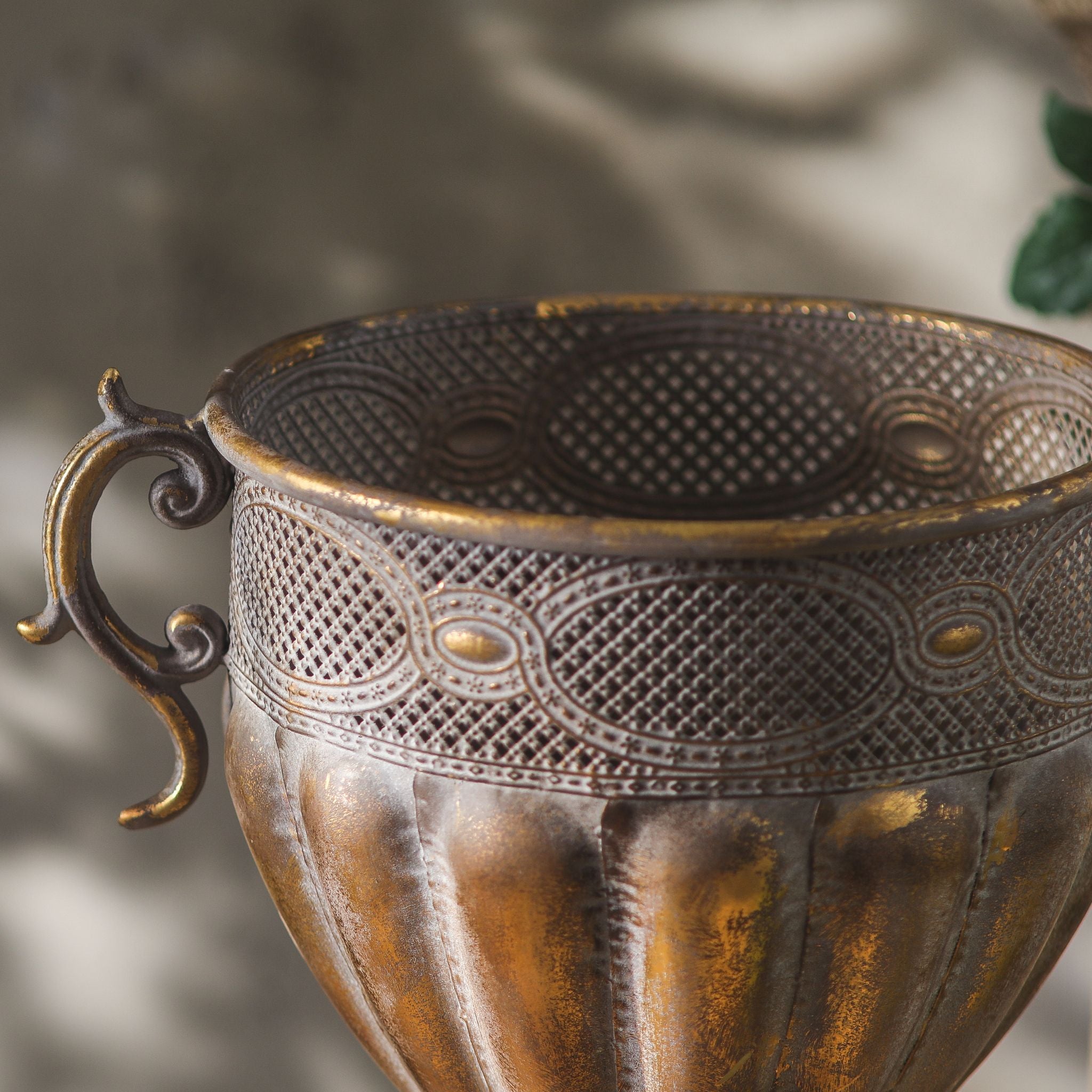 Close-up of the Benjamin urn pierced openwork band, scroll handle and rim in antique gold metal.