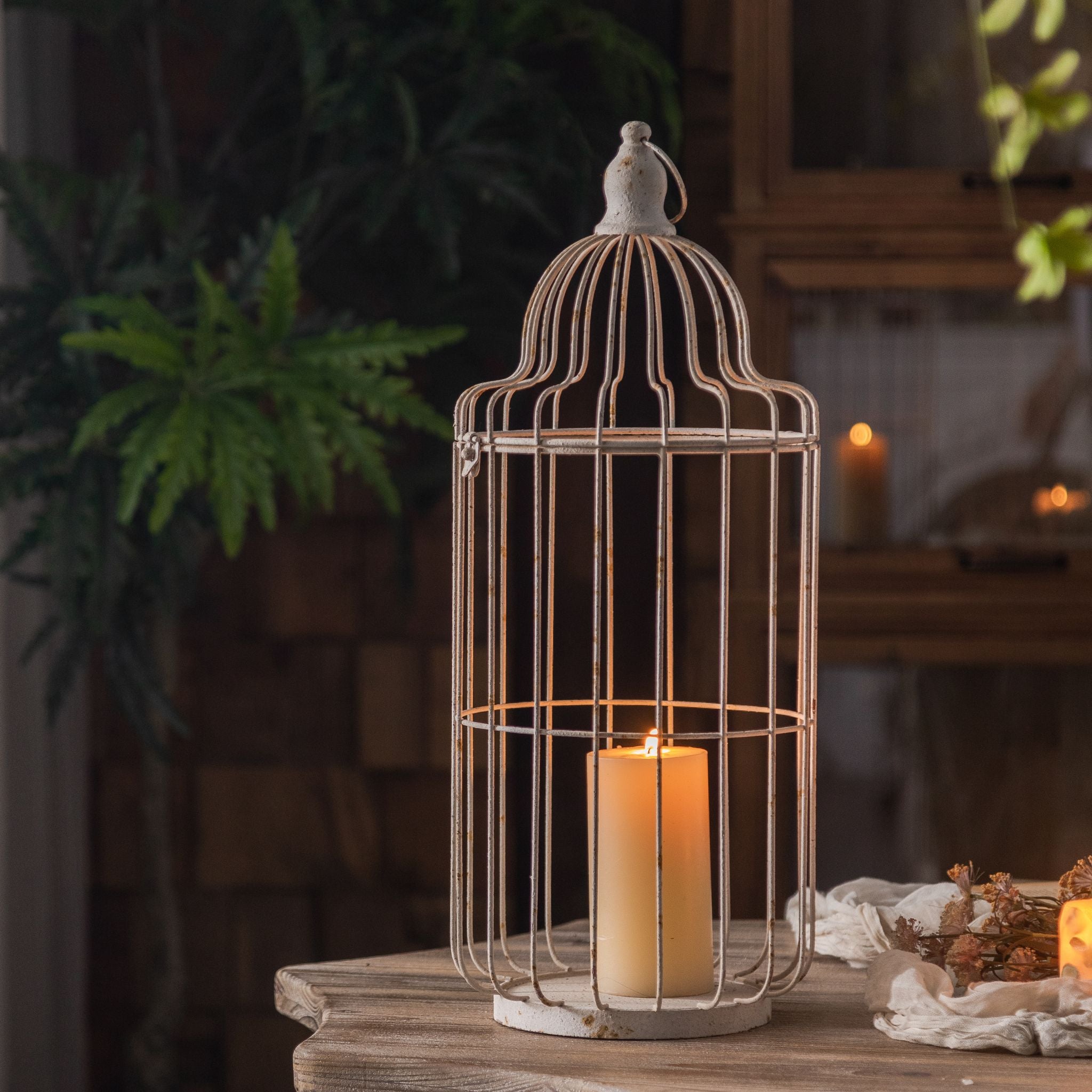 Bernard large birdcage candle lantern with lit pillar candle on dark wood styled with greenery