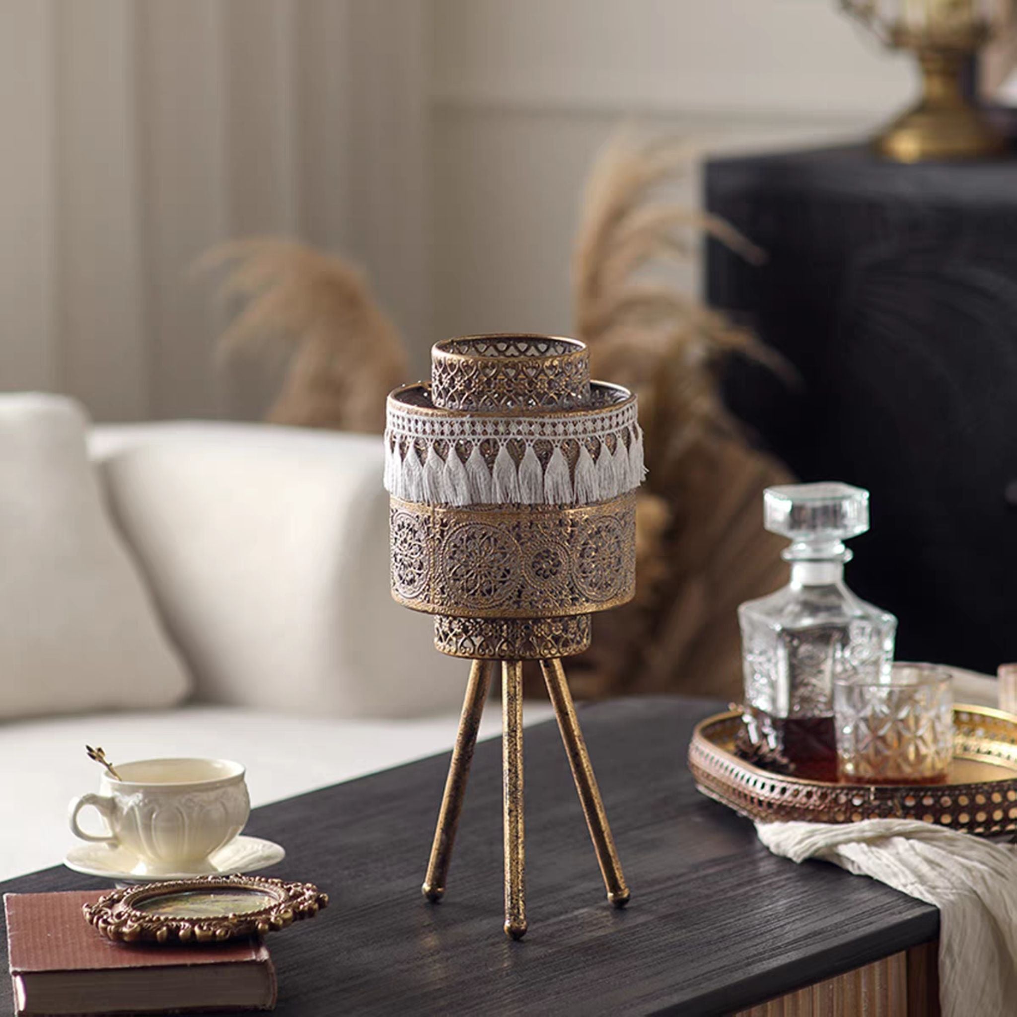 Leila boho tealight lantern on a tripod stand in antique gold with white tassel trim.