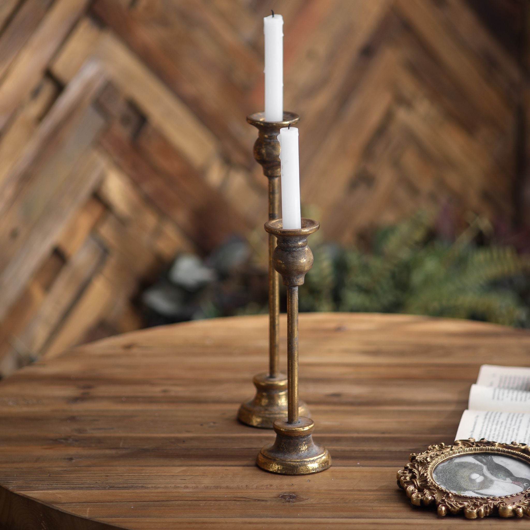 Karine French Provincial taper candlestick set, two aged gold metal holders of different heights with white taper candles on a timber table