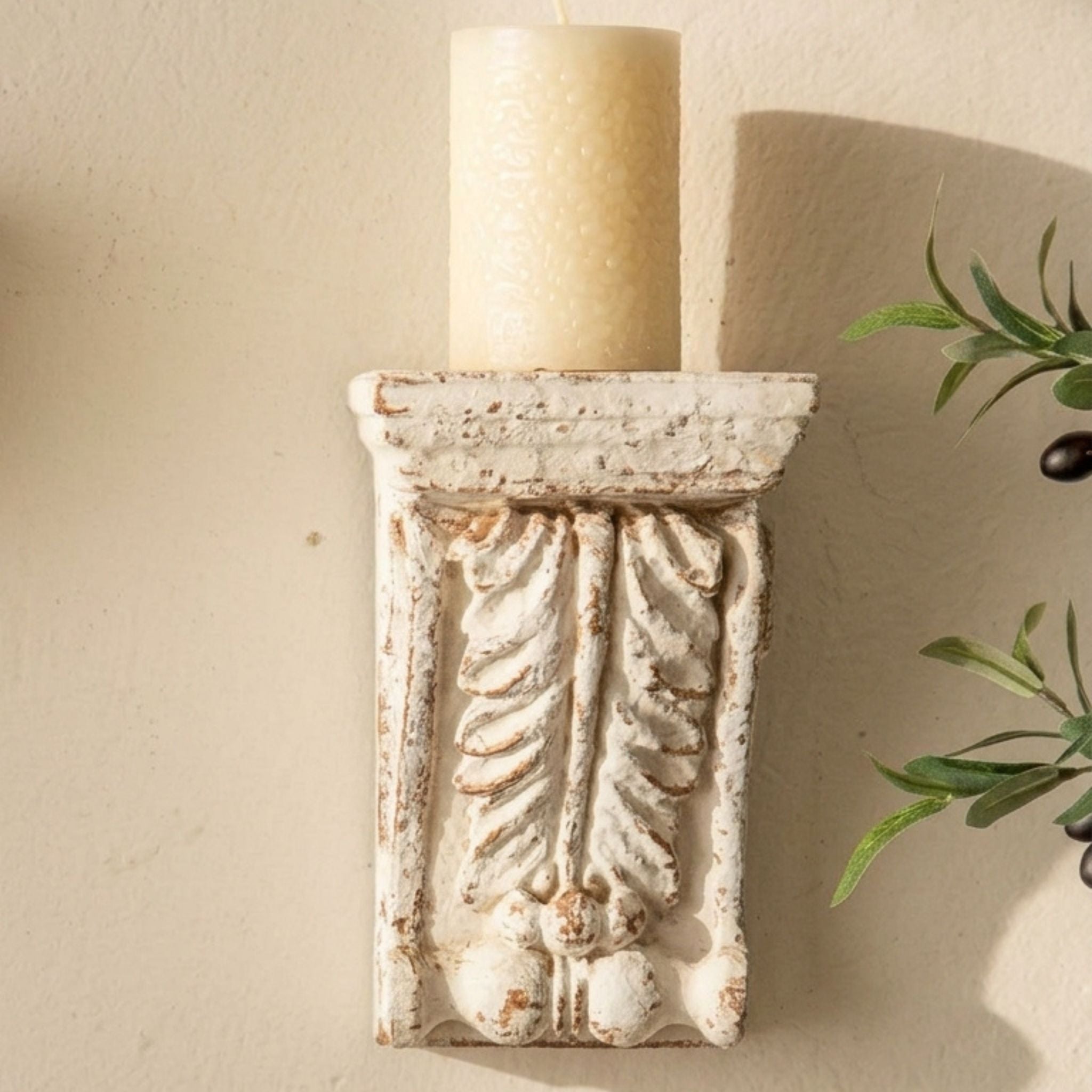Brigitte corbel wall sconce holding a cream pillar candle, styled with an olive sprig