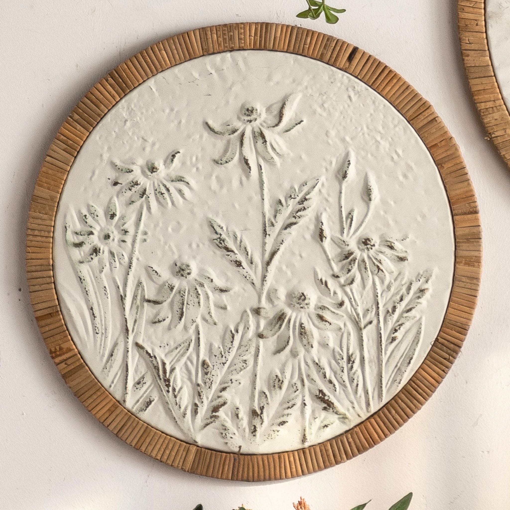 Calvin French Provincial round wall art, embossed meadow of daisy-like flowers in distressed white with a natural rattan frame.