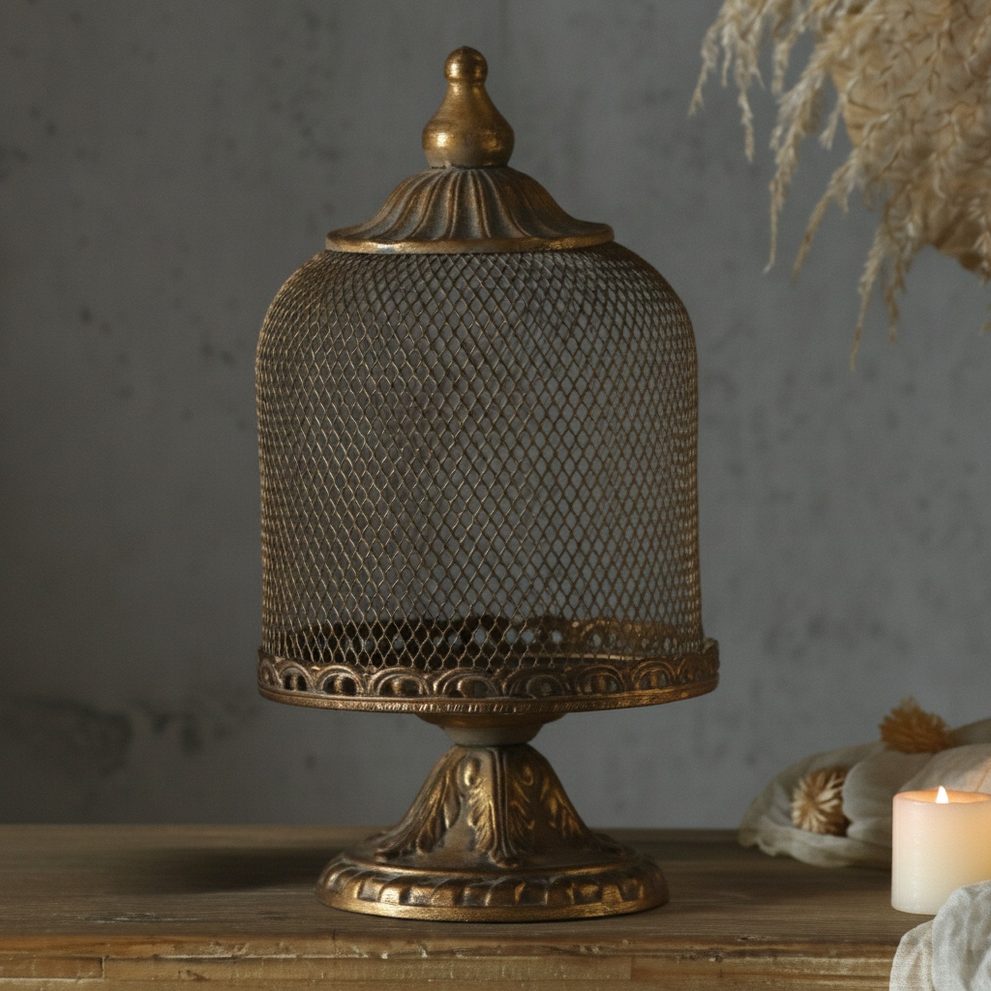Tall mesh cloche styled on a wooden console with dried stems and candlelight