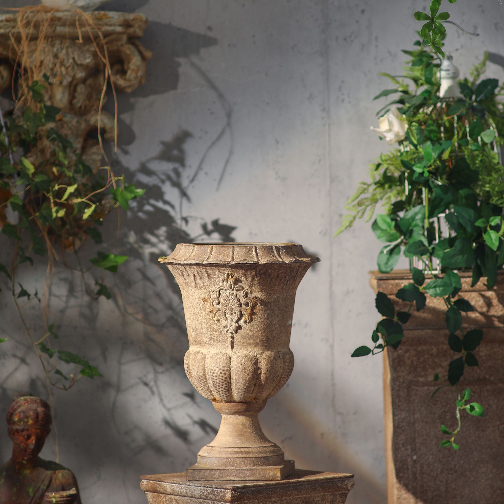 Delphine urn displayed on a stone plinth among trailing greenery