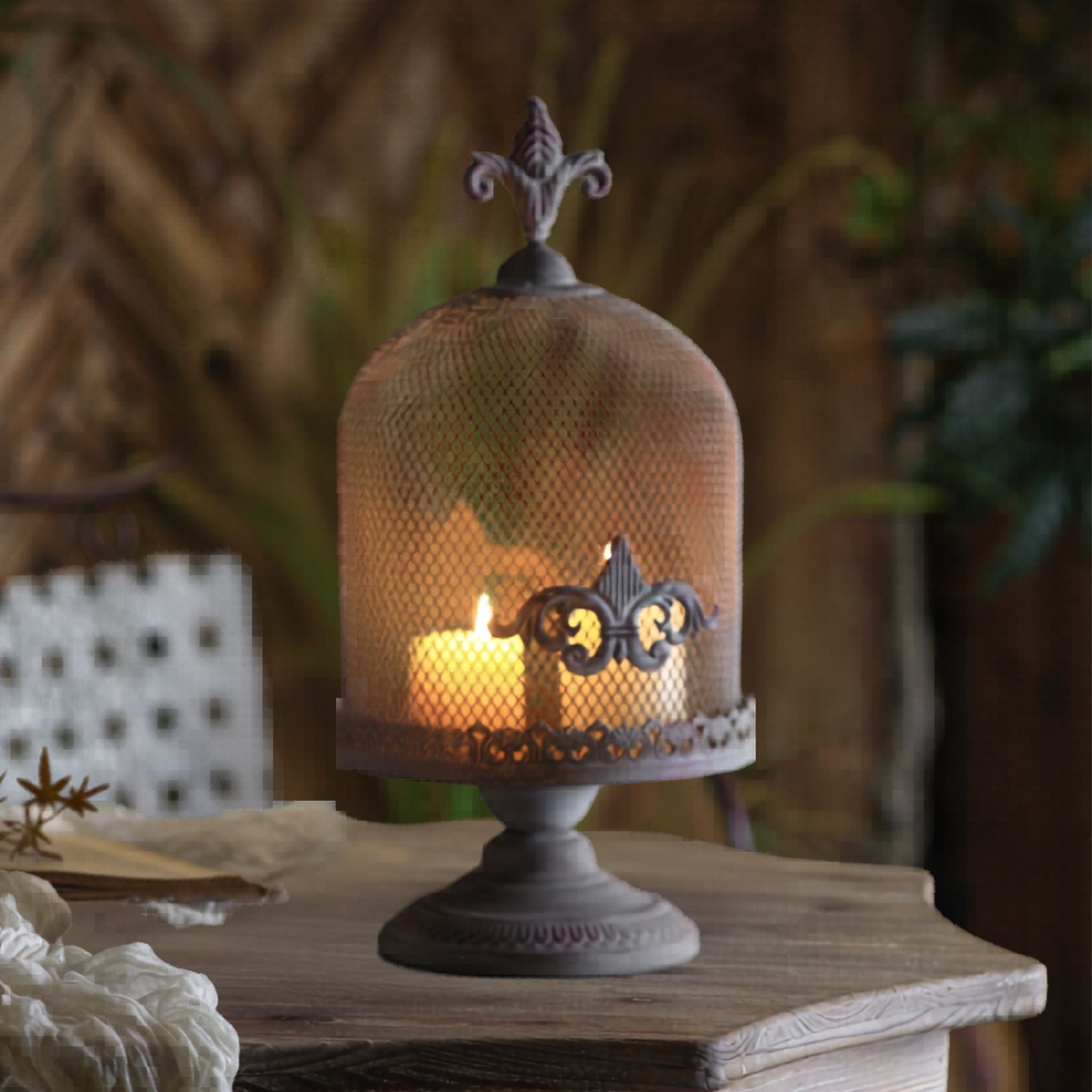 Cécile French Provincial candle cloche close-up showing aged iron mesh dome, fleur-de-lis finial and scrollwork over a lit pillar candle
