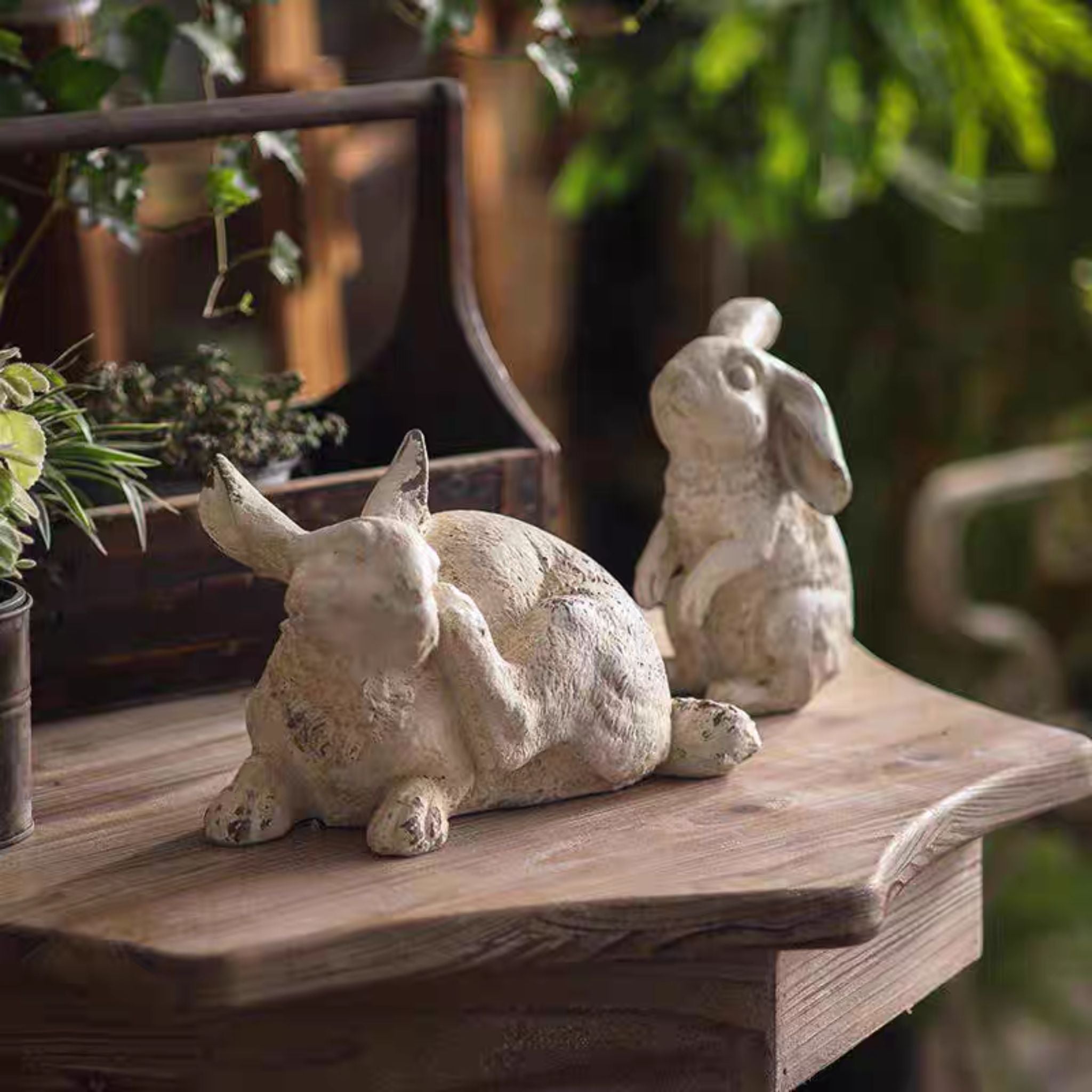Coco scratching rabbit statue styled with Pomme sitting tall rabbit on a wooden table with ferns