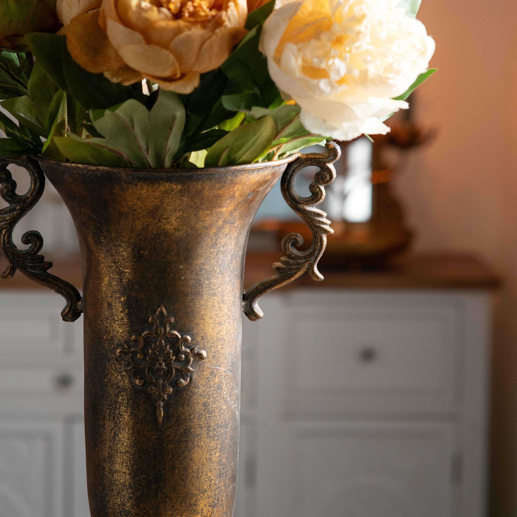 Close-up of the Coralie urn vase scroll handle and fleur-de-lis medallion in aged gold metal