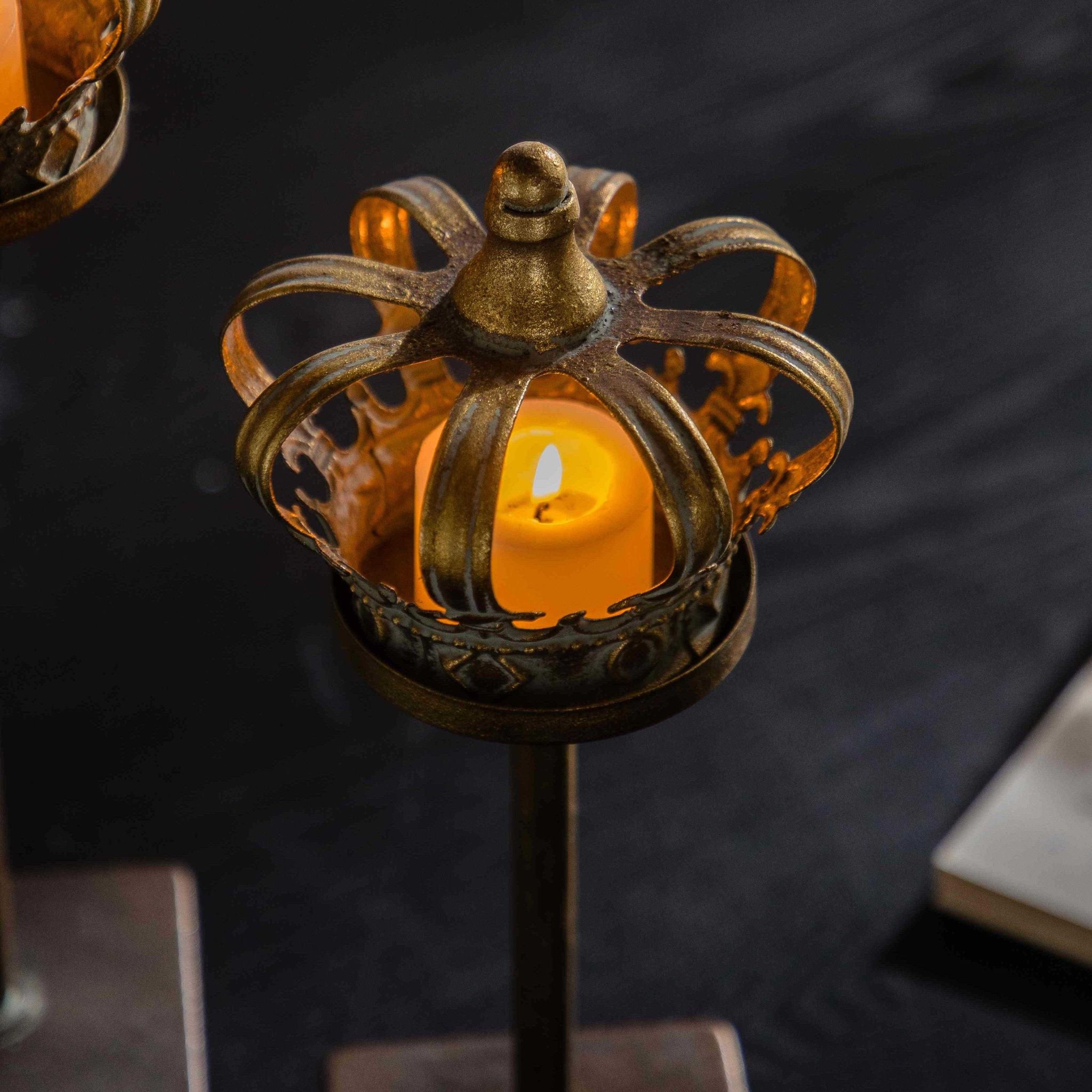 Close-up of a crown tealight holder with a lit tealight inside, antique gold bands and fleur rim.