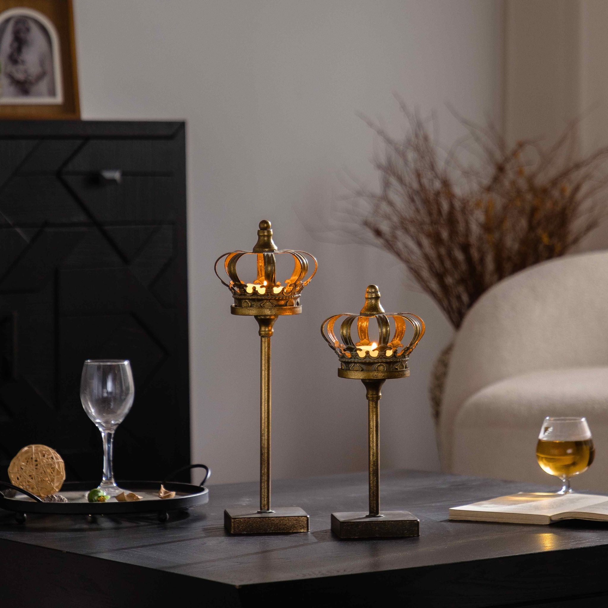 Two crown tealight holders lit with tealights glowing through the openwork antique gold crowns.