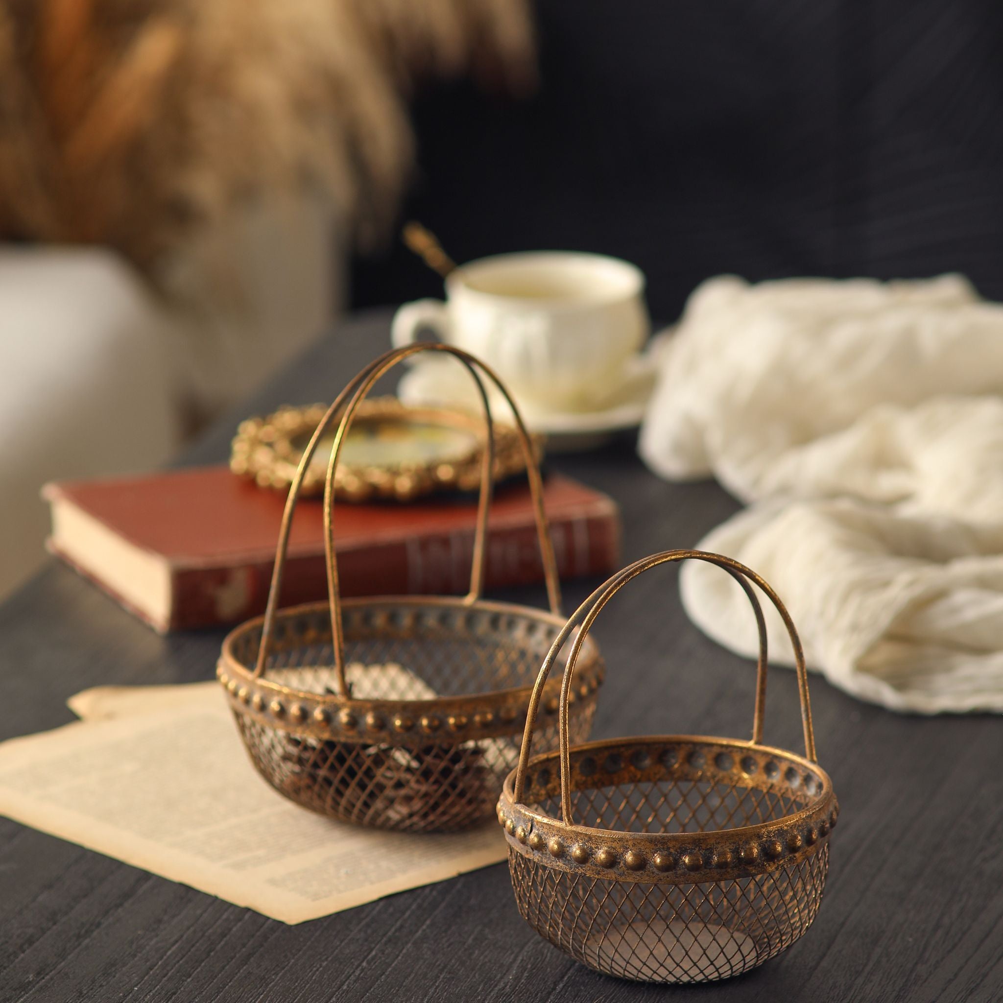 Diane antique gold wire basket pair styled on a dark table with a teacup and book, showing both sizes.